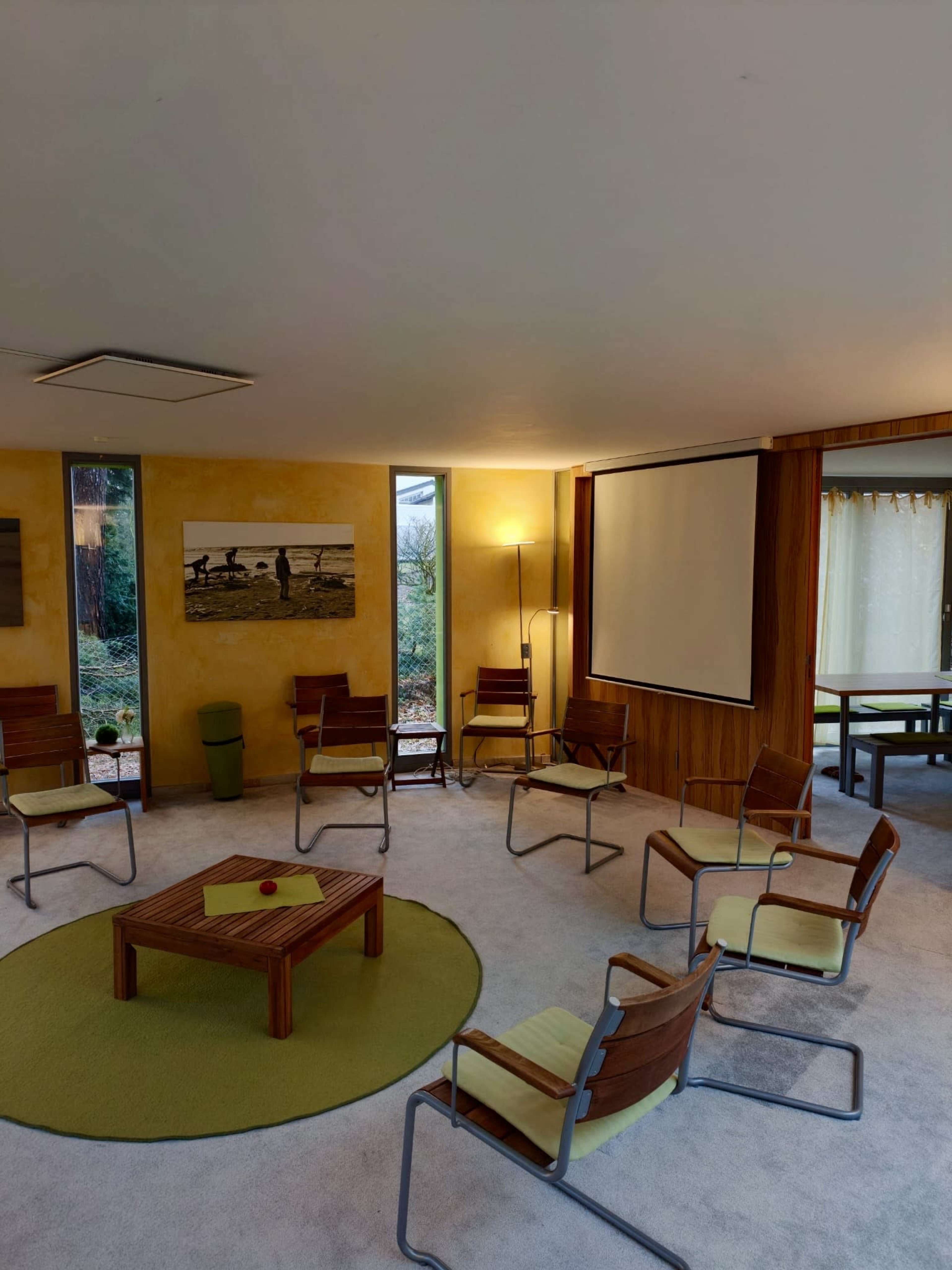 The image shows a modern meeting room with circular seating arranged around a small wooden table on a green rug.