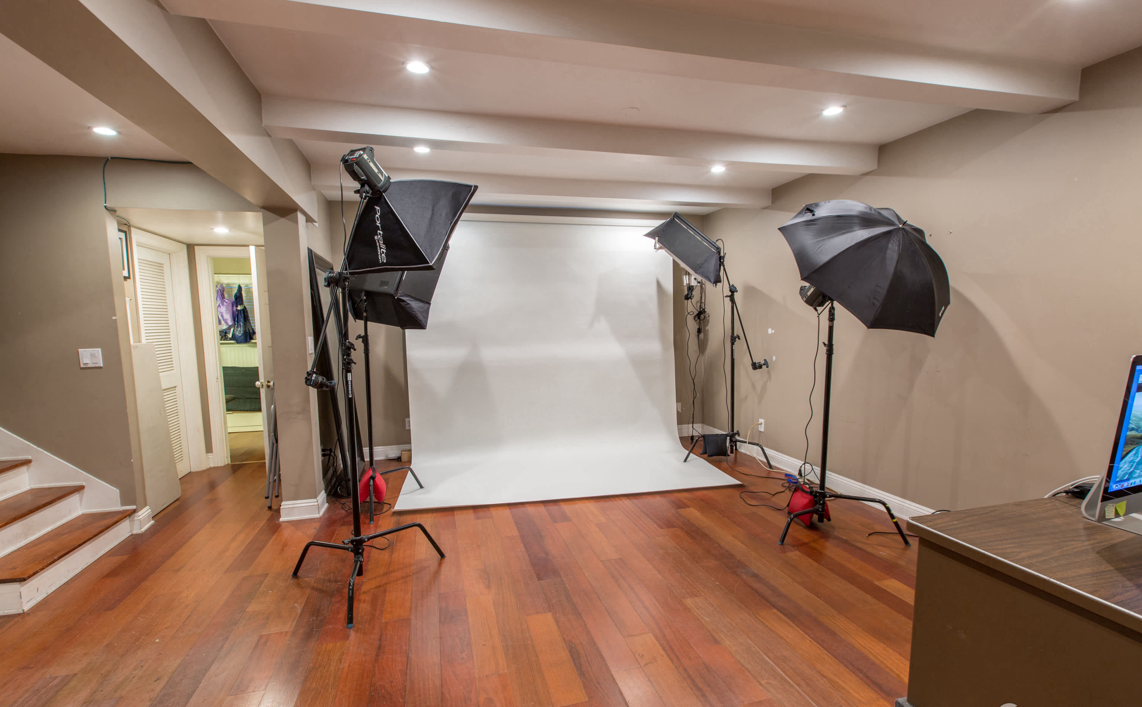 A photography studio with a blank backdrop and three light stands set up on a wooden floor.