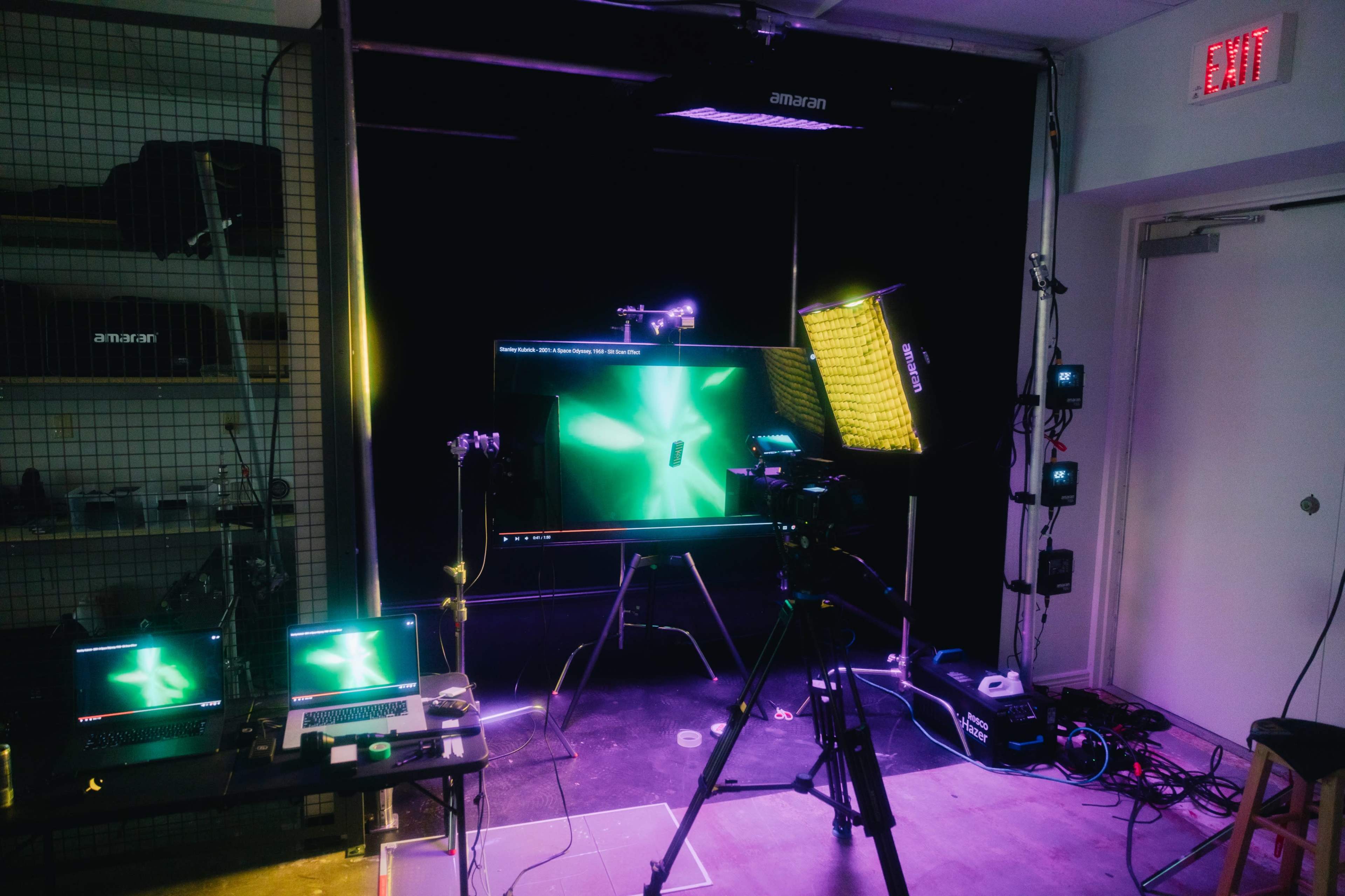 A tech setup in a studio with multiple screens, cameras, and lighting equipment arranged around a central display.