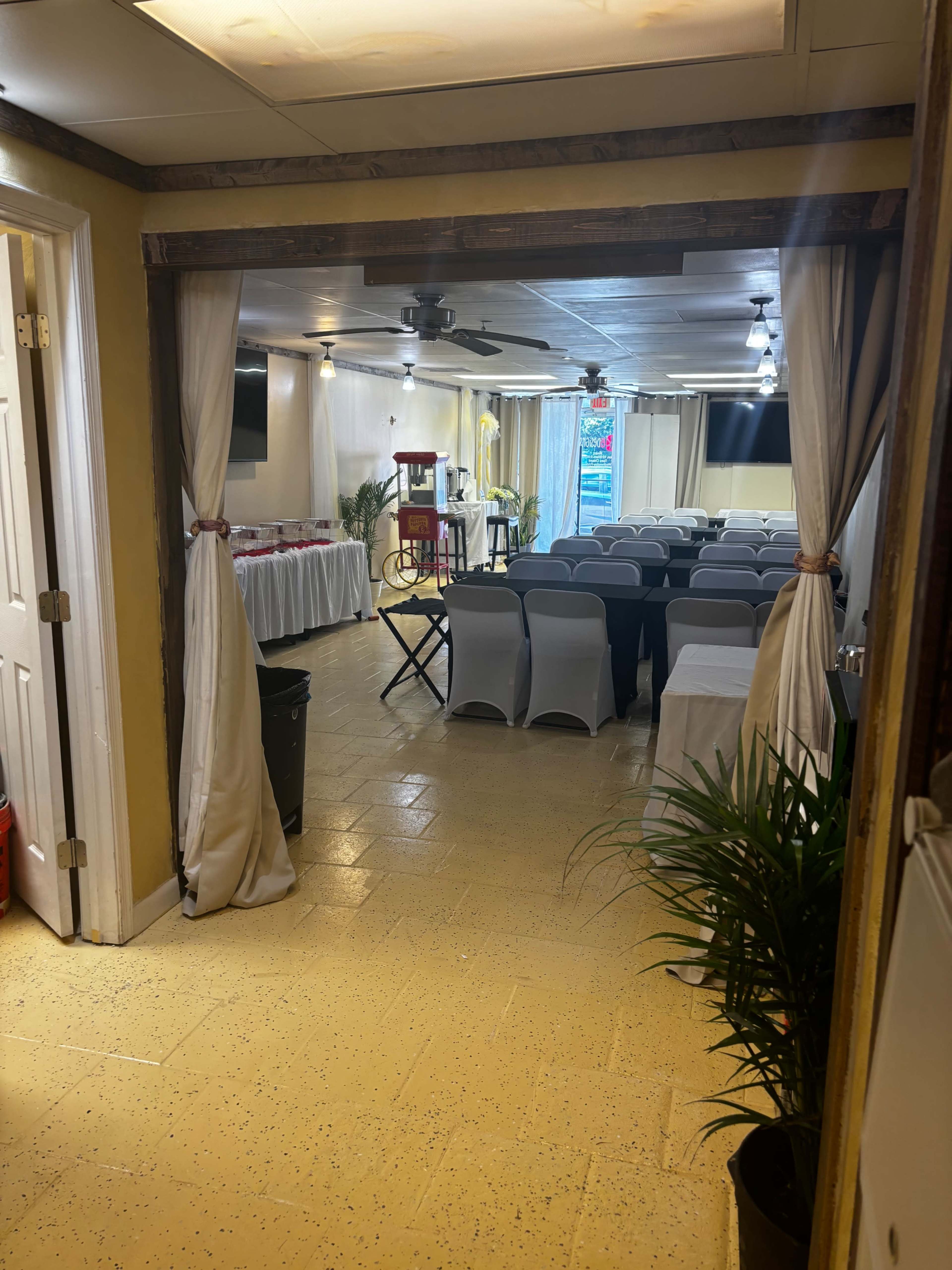 The image shows a conference room setup with rows of chairs, a refreshment table, and large screens in a well-lit space.