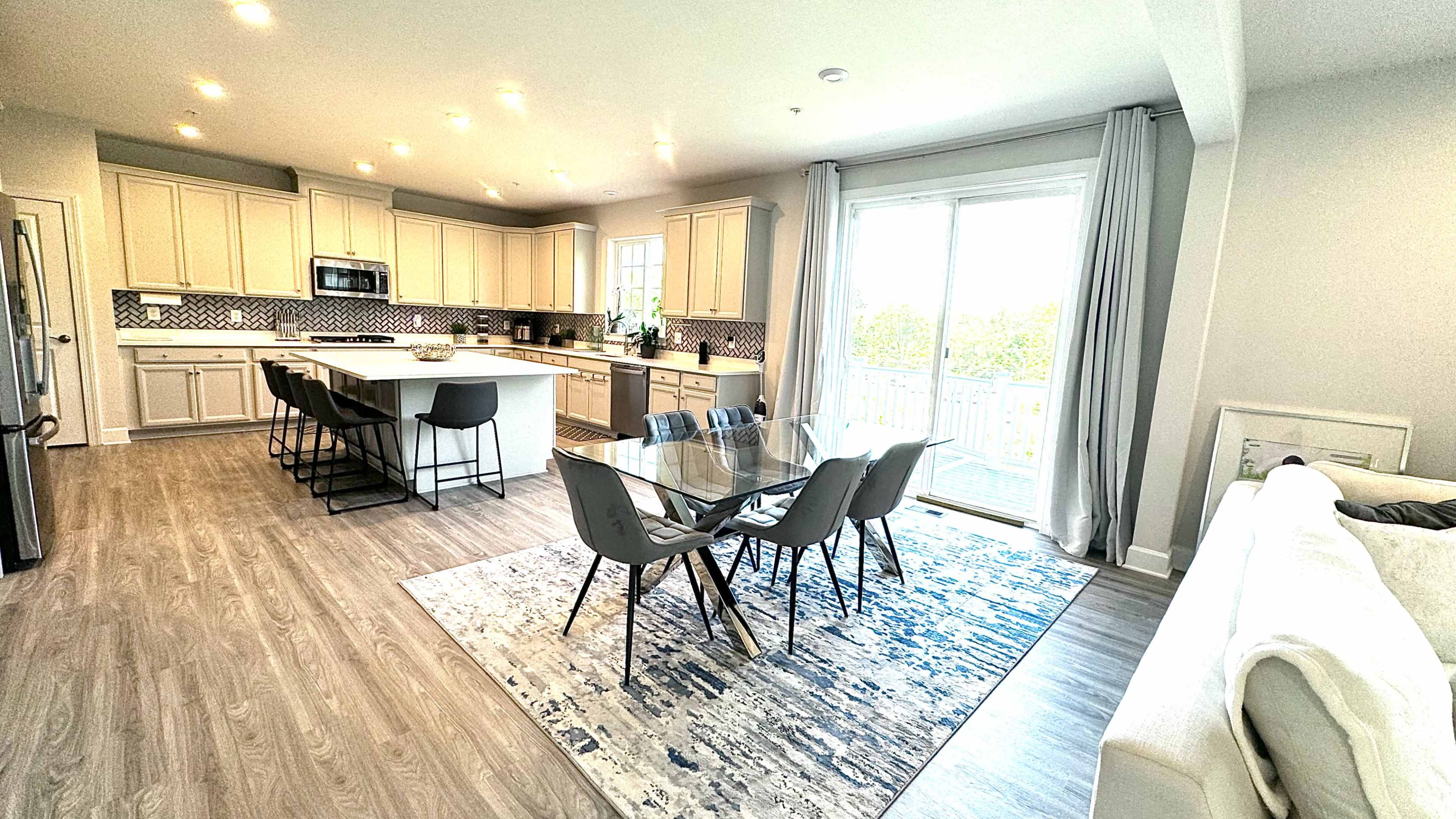 A modern open-concept kitchen and dining area with a large table and gray chairs, alongside a living space featuring a couch.