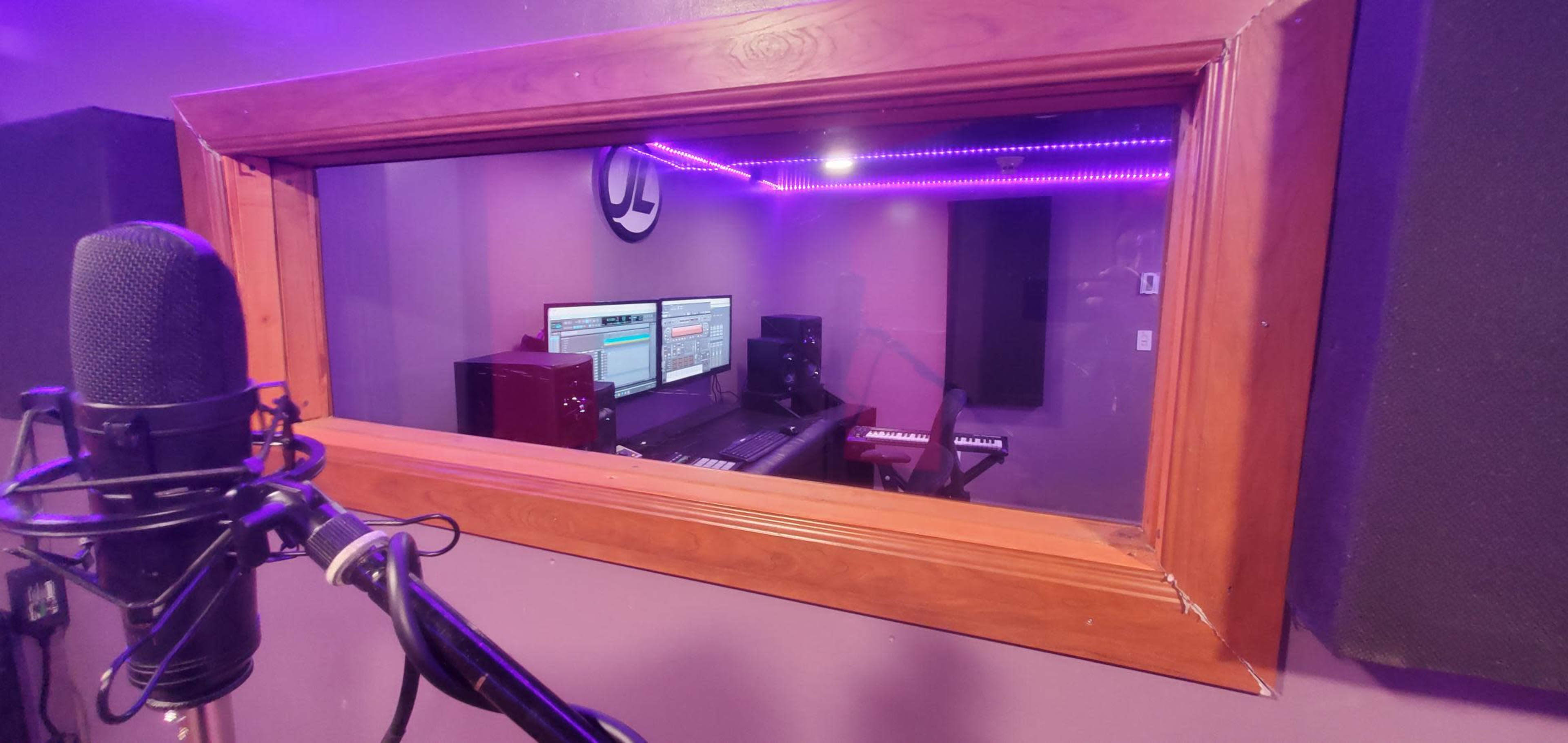 A recording studio is visible through a window, featuring a computer, mixing equipment, and musical instruments.