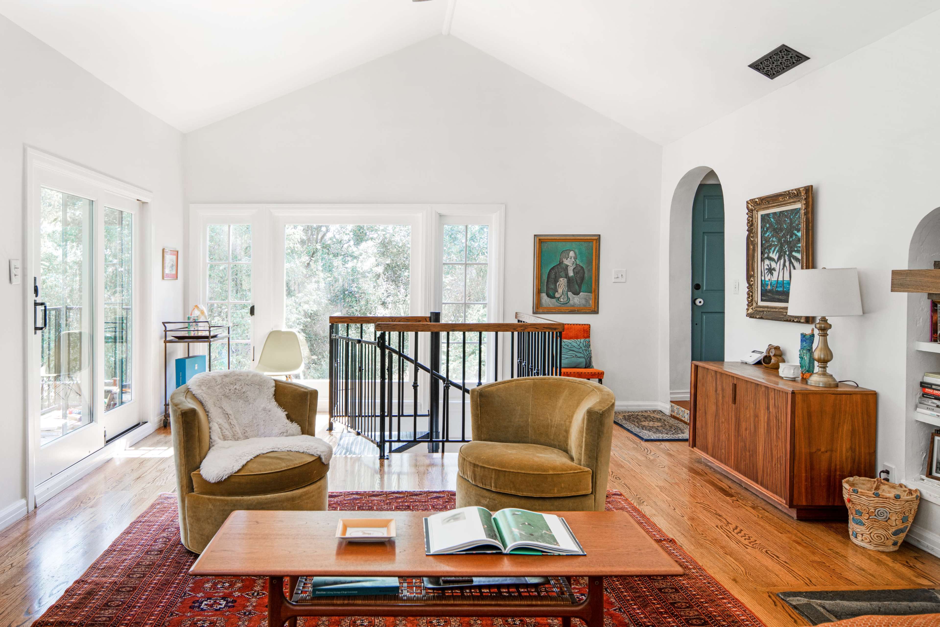The image shows a bright living room with two yellow armchairs, a wooden coffee table, and large windows that provide ample natural light.