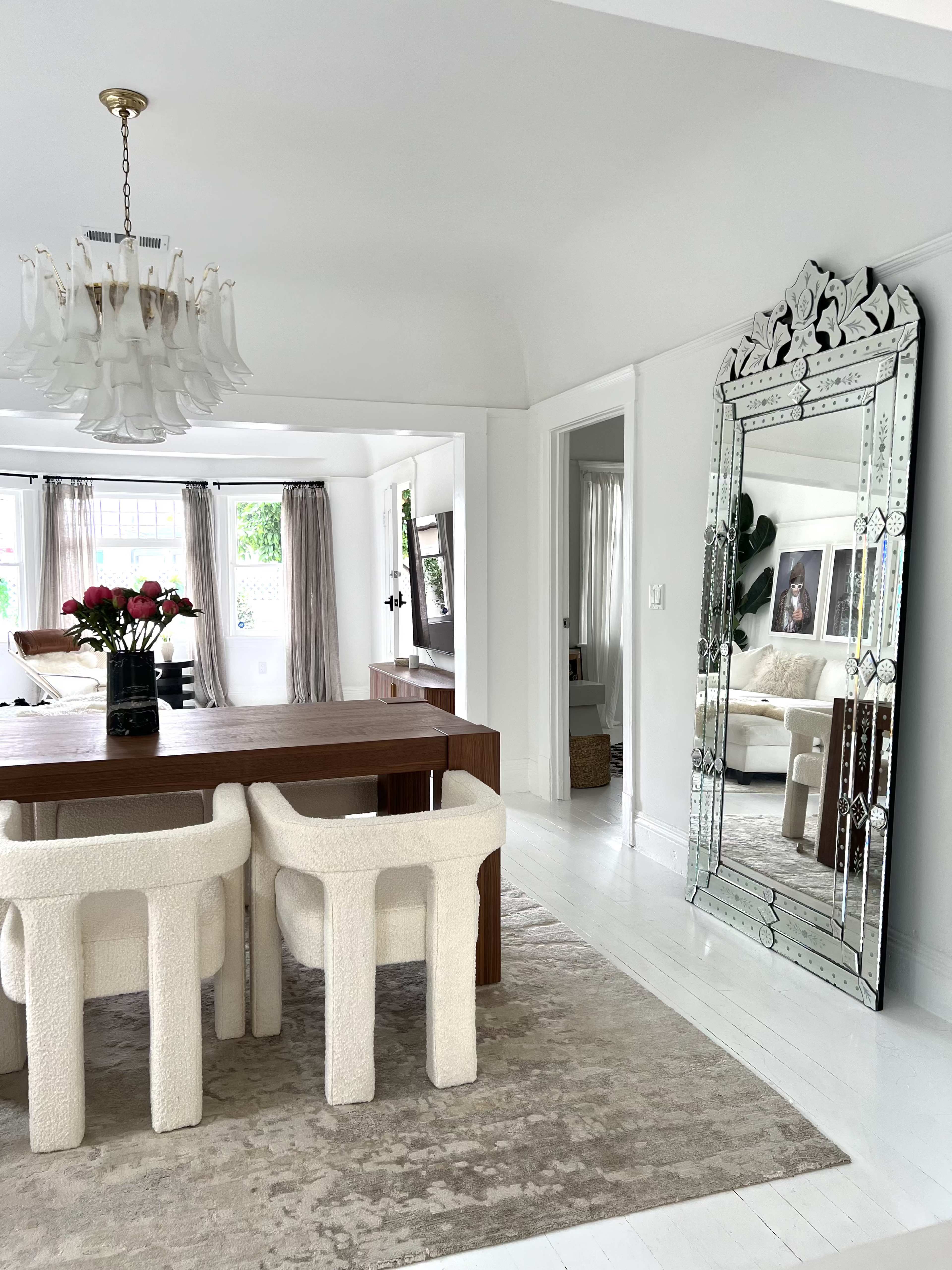 A dining area features a wooden table with upholstered chairs and a large decorative mirror against a light-colored wall.