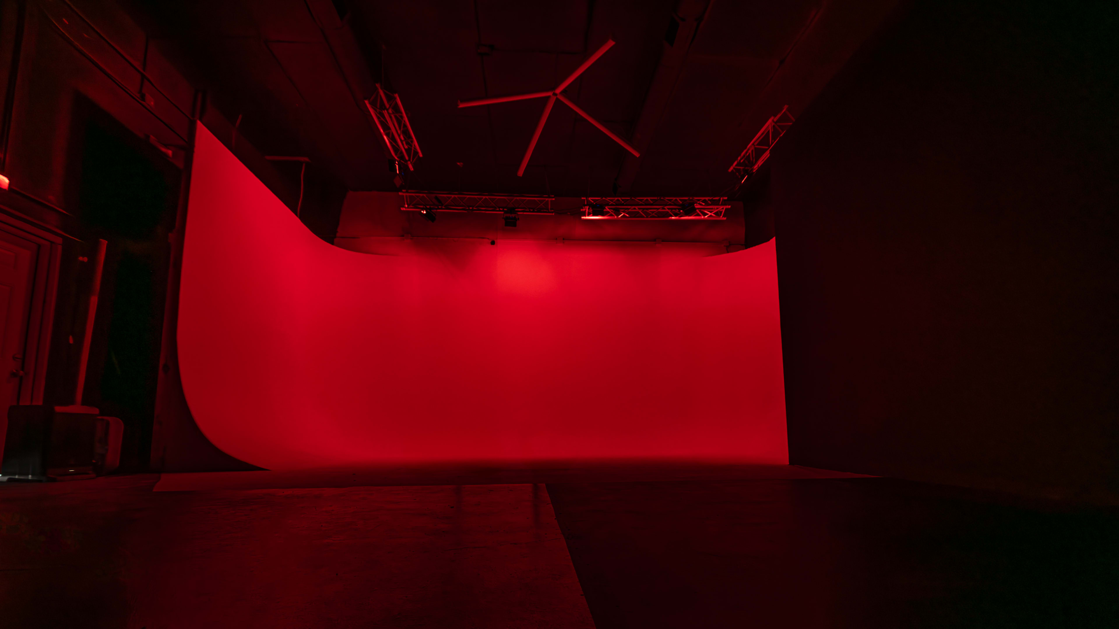 A photography studio features a large, seamless red backdrop illuminated by soft lighting.