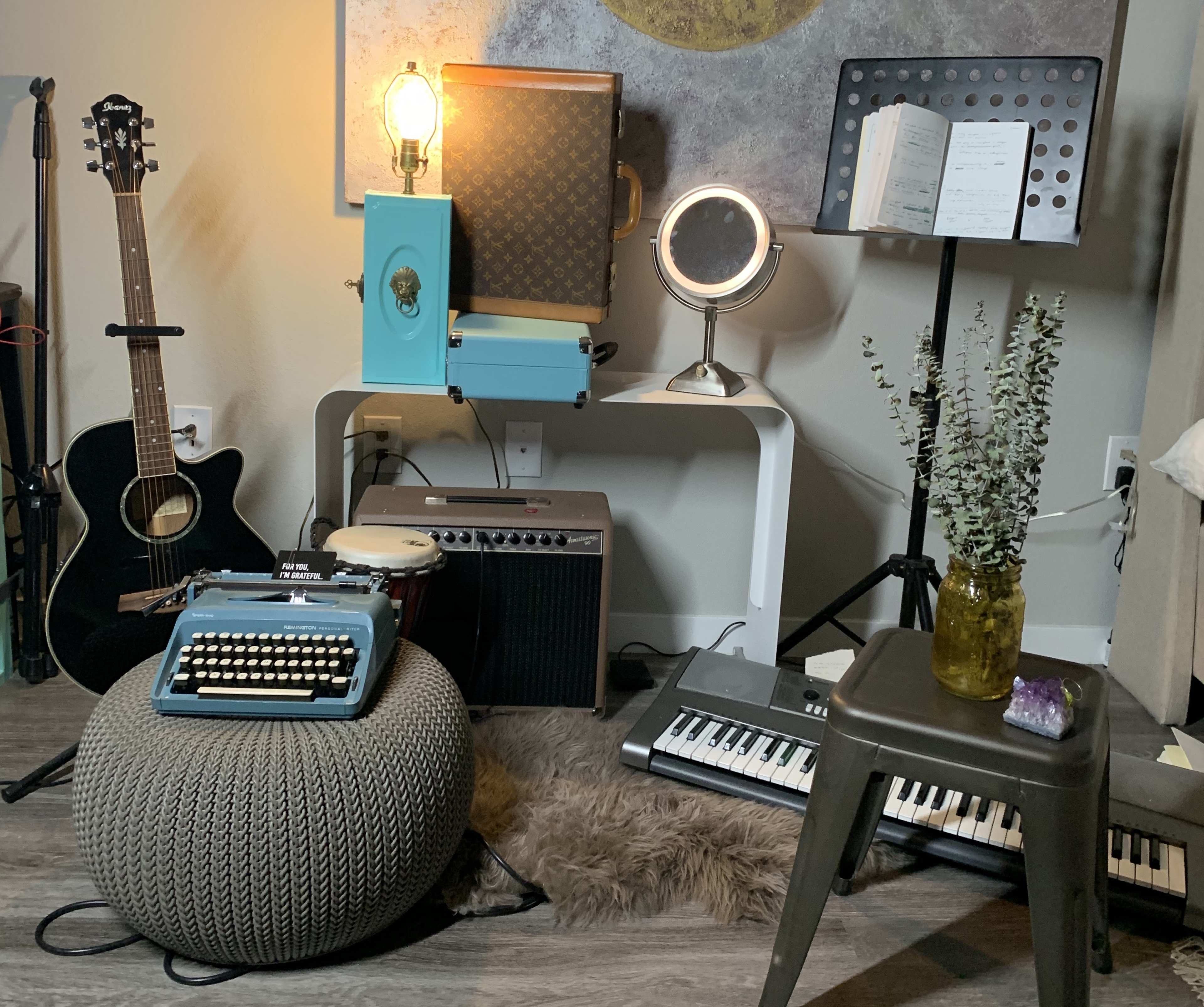A cozy corner includes a guitar, vintage typewriter, amplifier, keyboard, and decorative elements arranged around a pouf and side table.