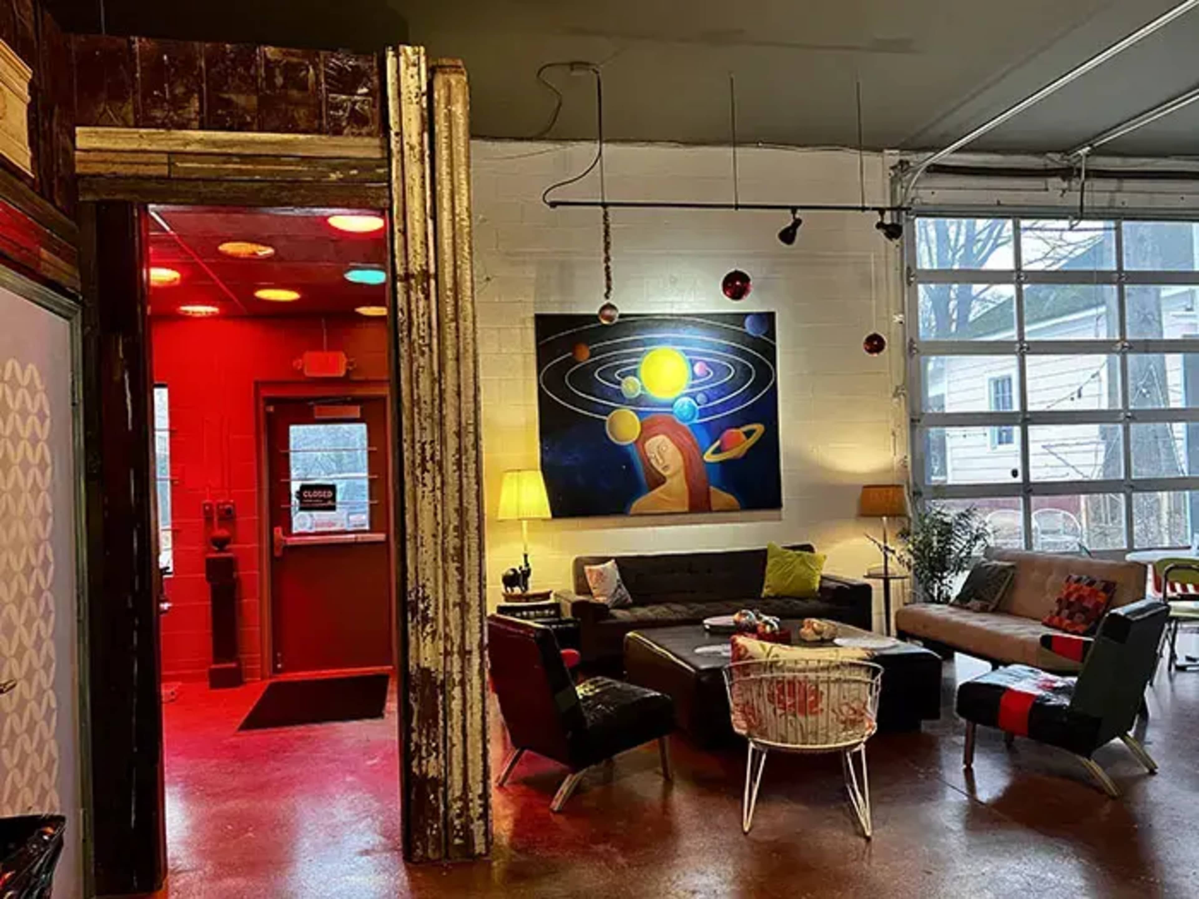 The image shows a colorful interior space featuring an art piece of the solar system on the wall, cozy seating arrangements, and a doorway leading to another area.