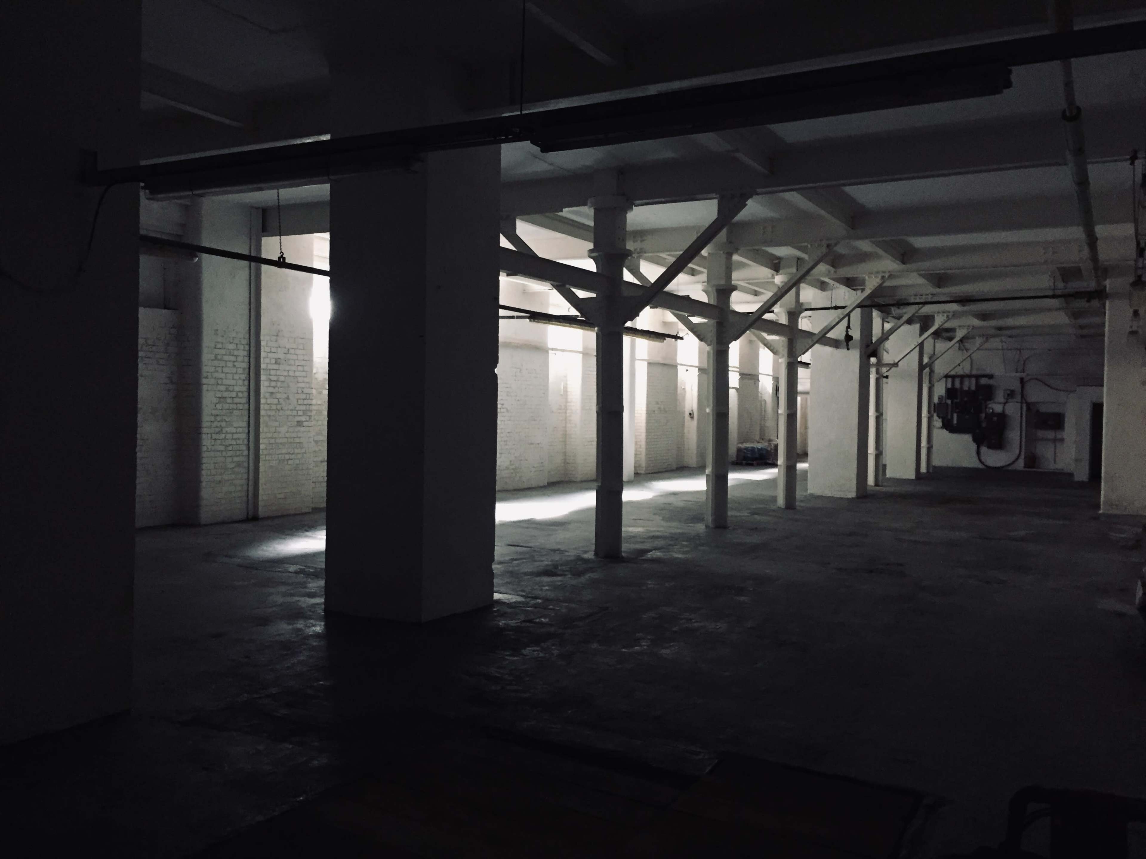 An empty warehouse with exposed beams and columns, illuminated by beams of light.