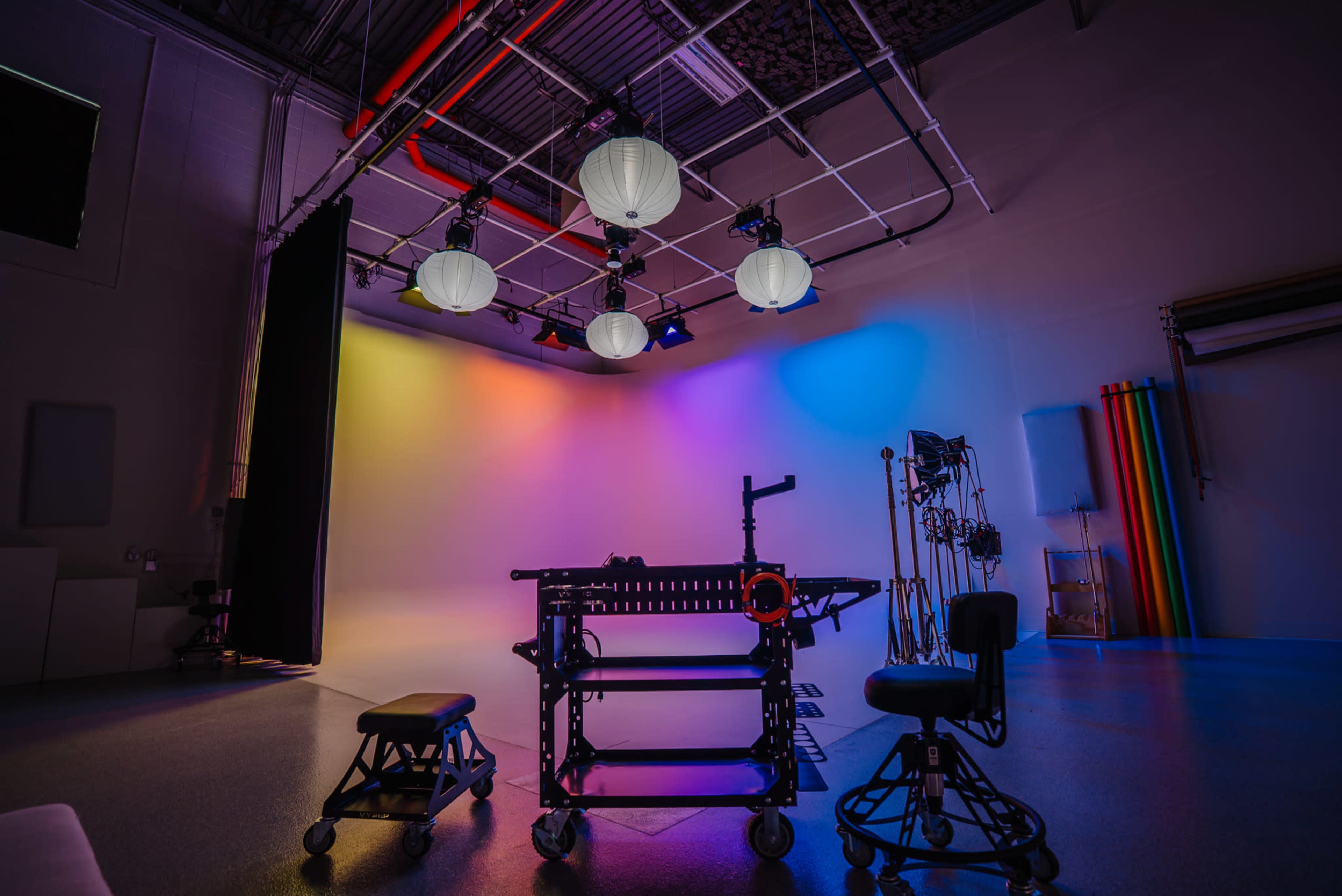 The image shows a well-lit studio space featuring a colorful backdrop, a motion control rig, and two empty chairs.