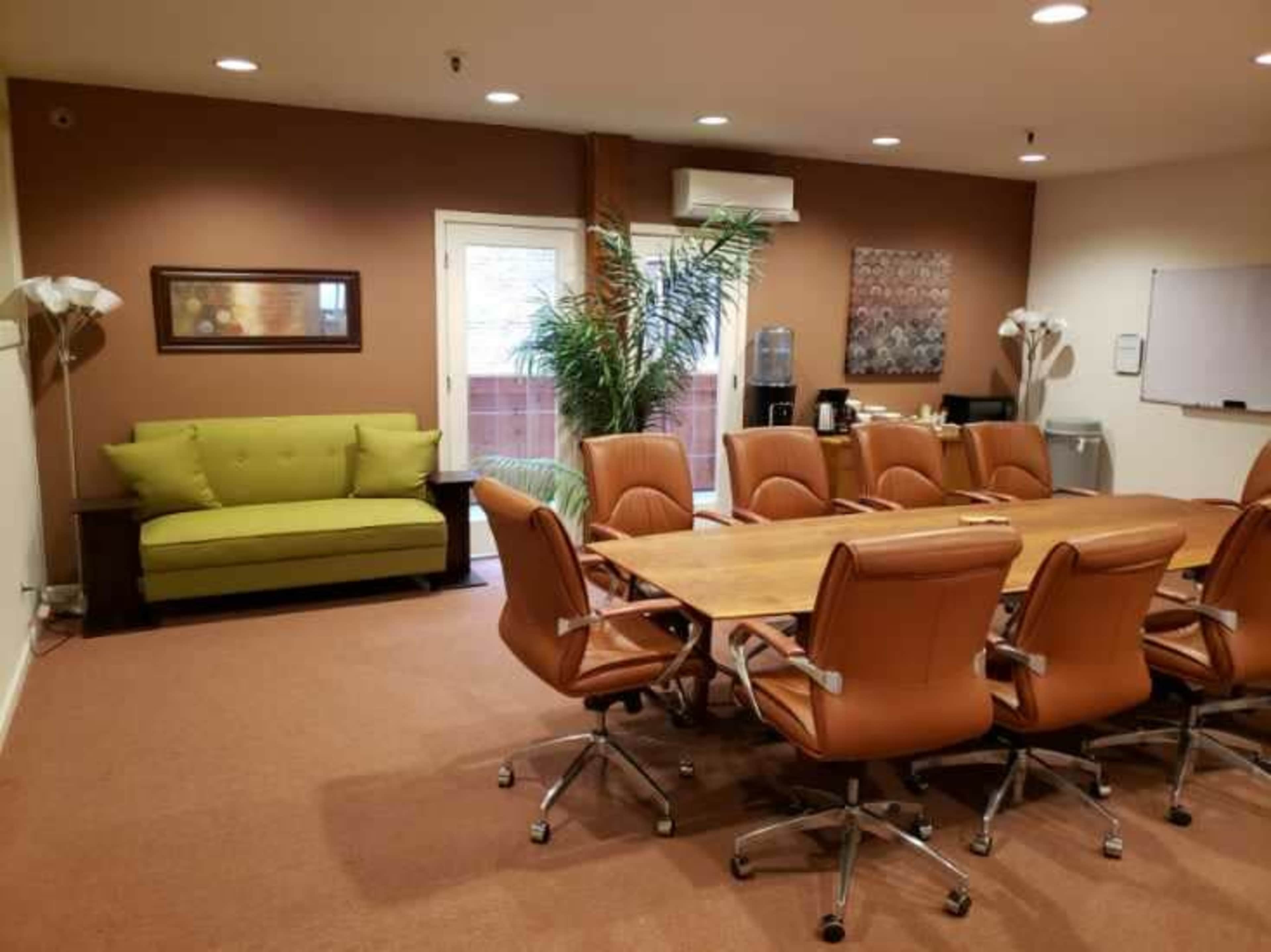 A conference room with a large wooden table surrounded by brown leather chairs, a green couch, and a whiteboard on the wall.