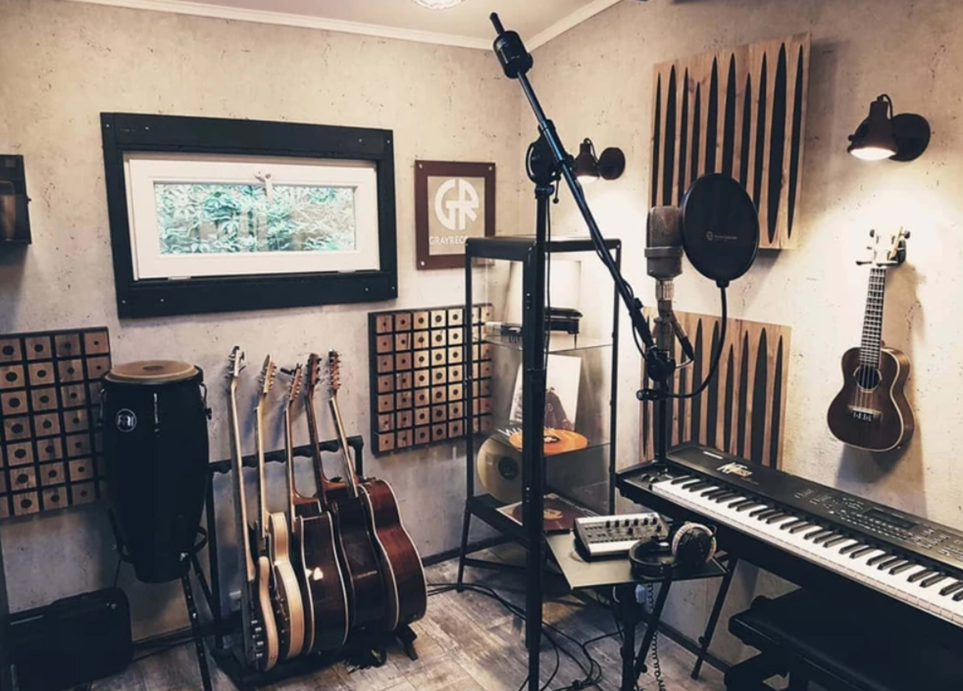 The image shows a well-equipped music studio featuring various instruments, including guitars, a ukulele, and a keyboard, along with a microphone on a stand and soundproofing panels on the walls.