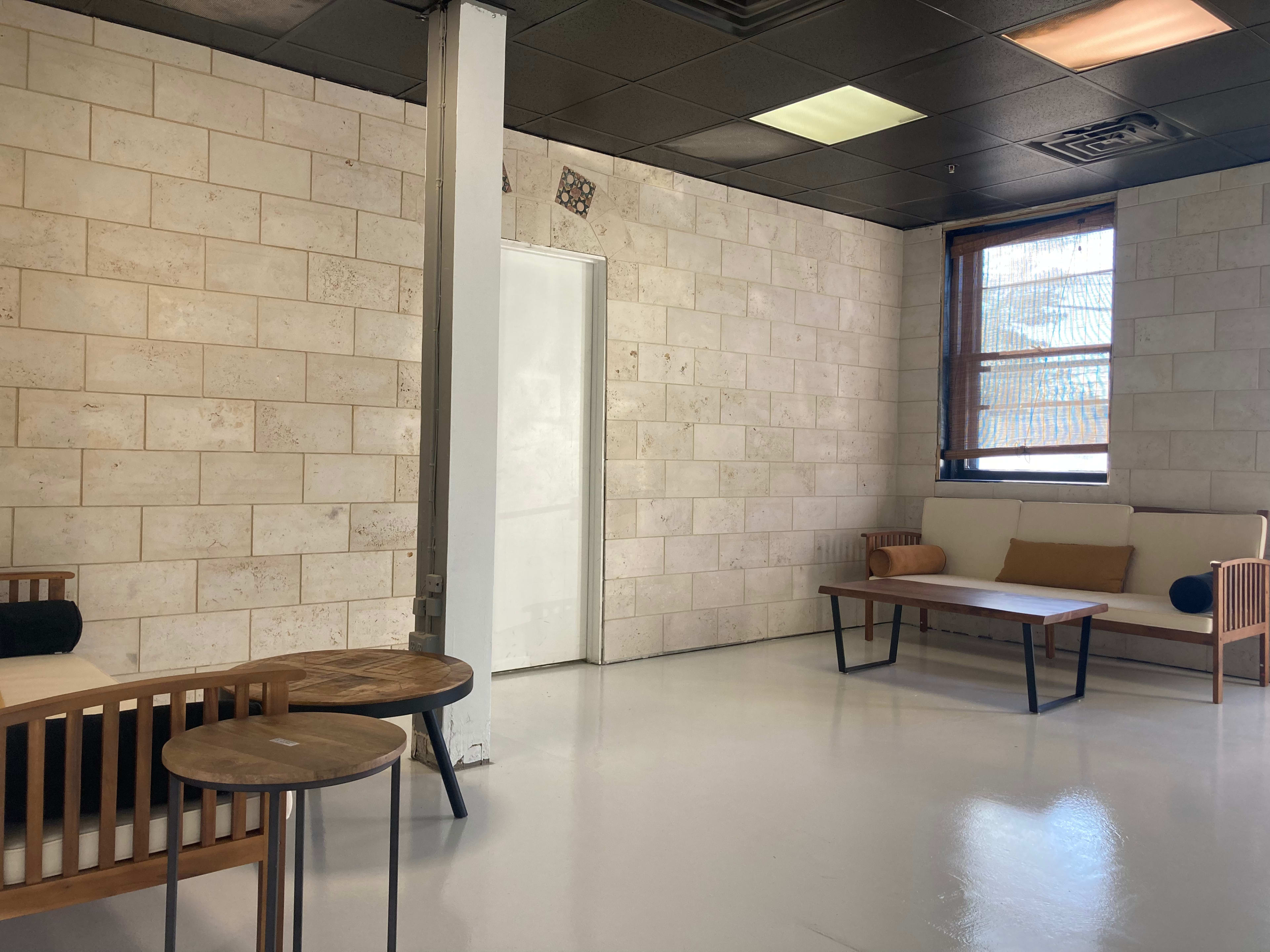A minimalist interior space with light-colored stone walls, two wooden seating areas, a coffee table, and a single door in the background.