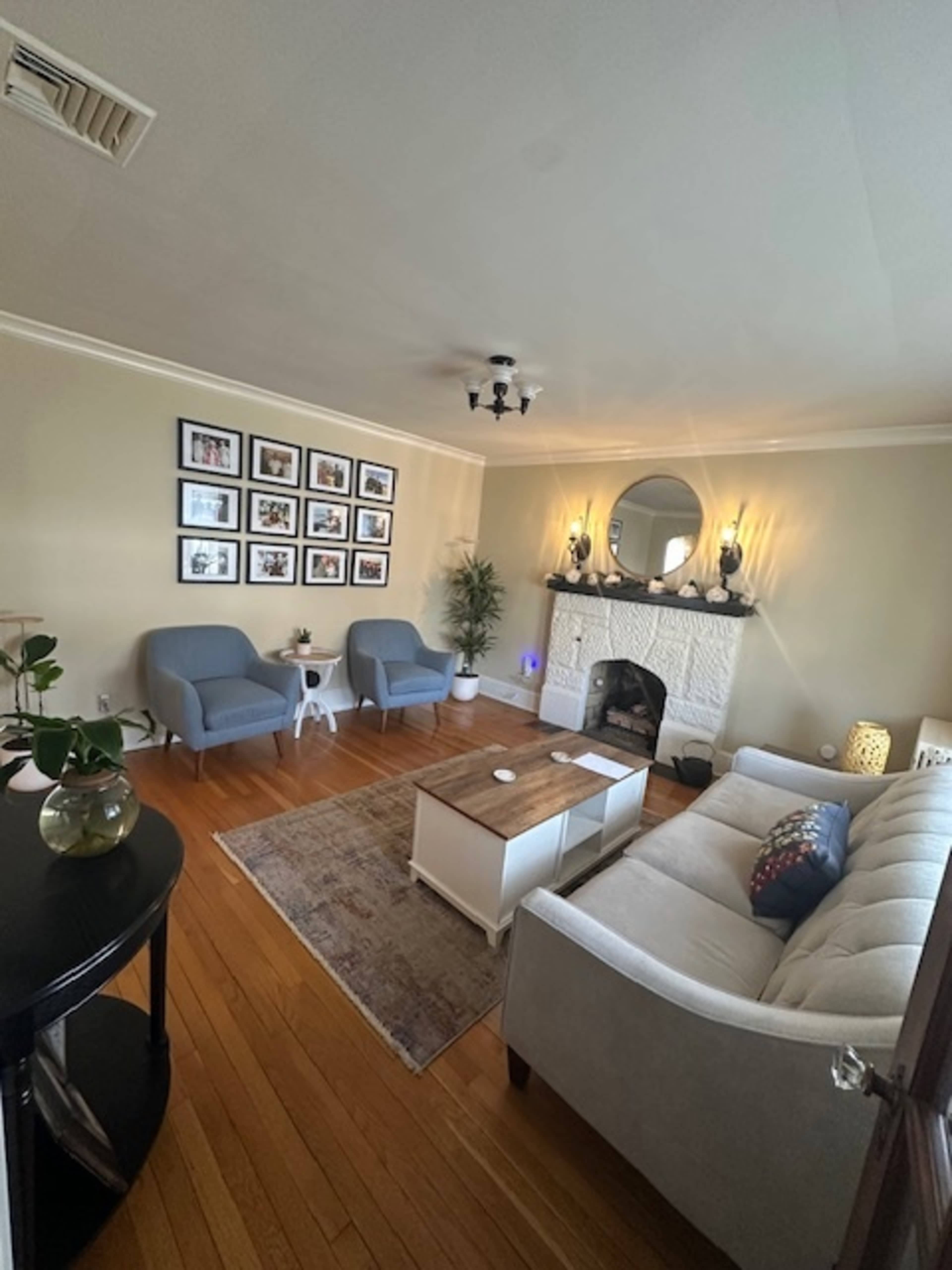 The living room features a plush sofa, two armchairs, a coffee table, and a framed photo gallery on the wall, with a fireplace as a focal point.