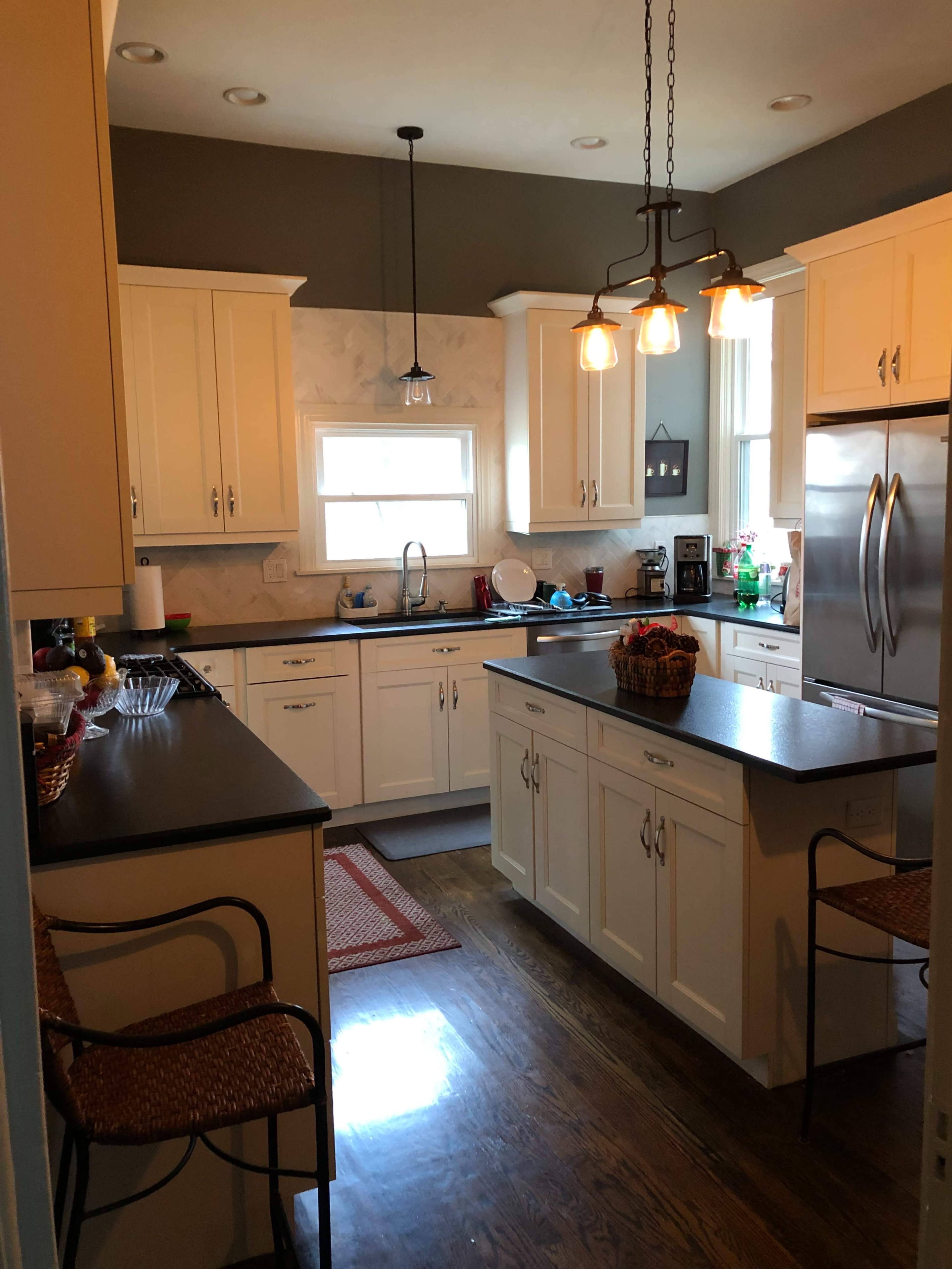 A modern kitchen with white cabinets, a central island, and warm lighting fixtures.