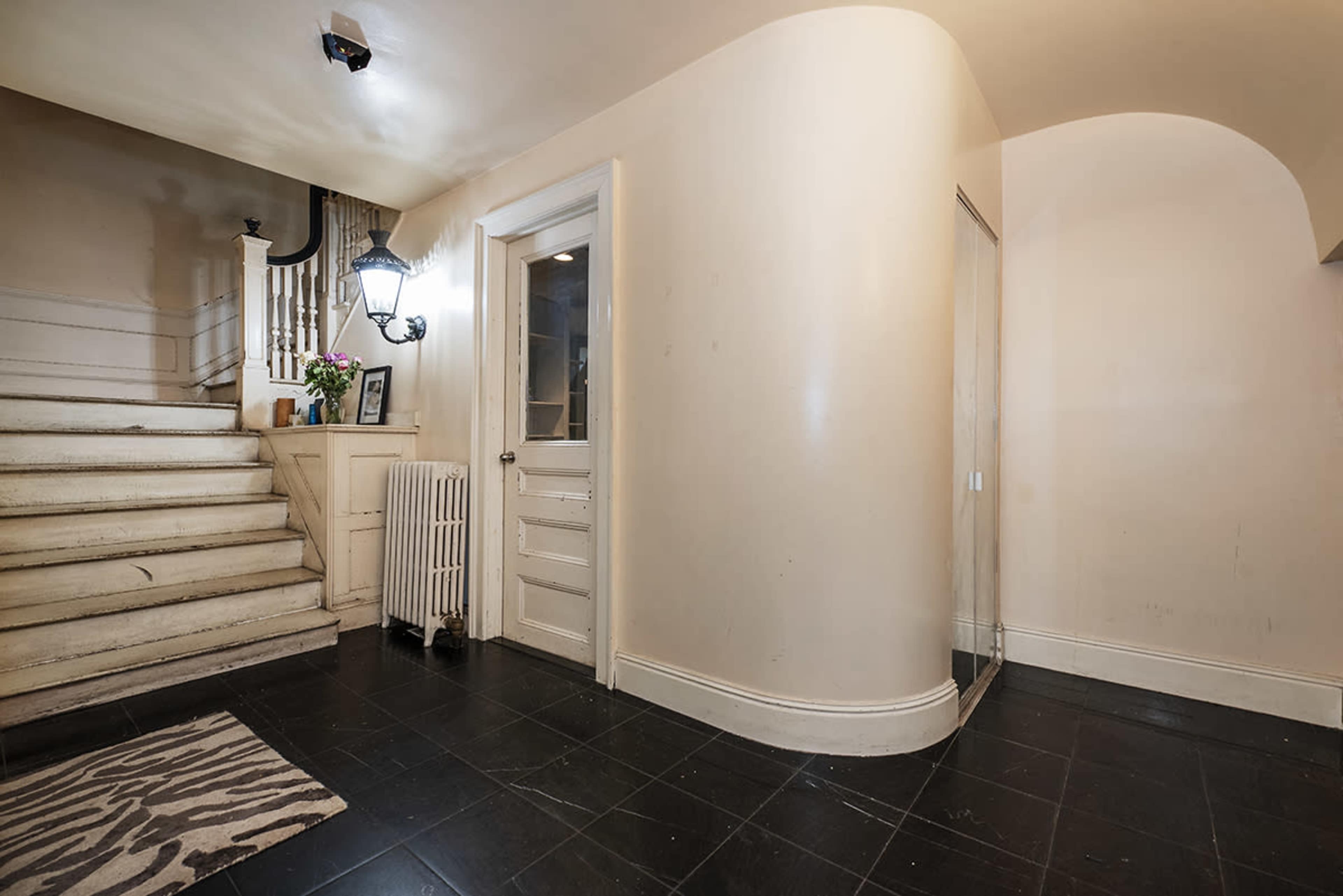 A hallway with a curved wall, a white staircase, a glass shower enclosure, and a door leading to another room.