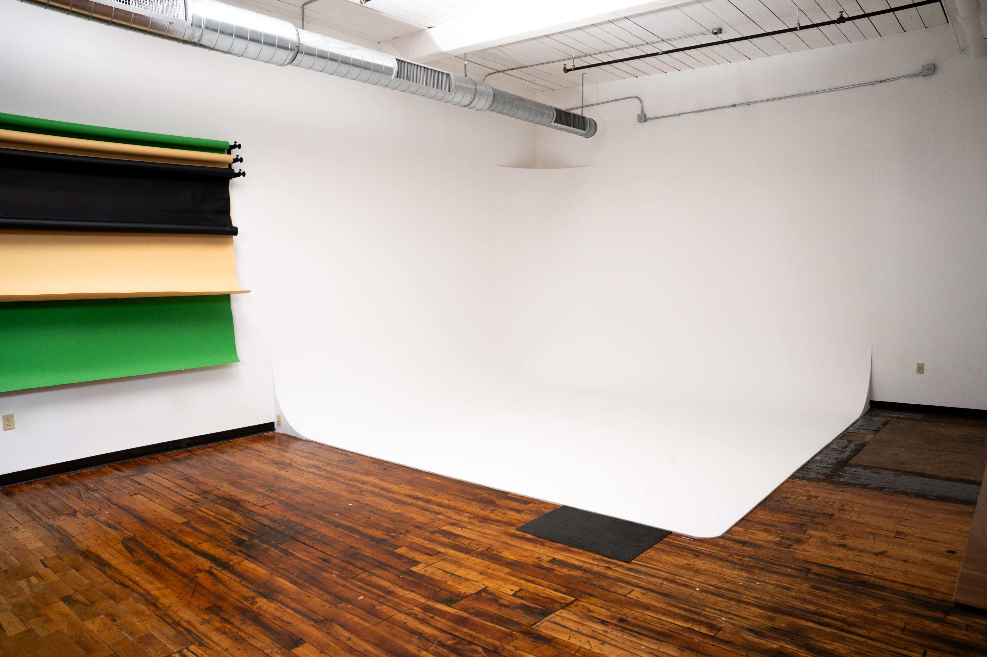 A spacious studio with a seamless backdrop of white and colored backdrops hanging on the wall, along with wooden flooring.