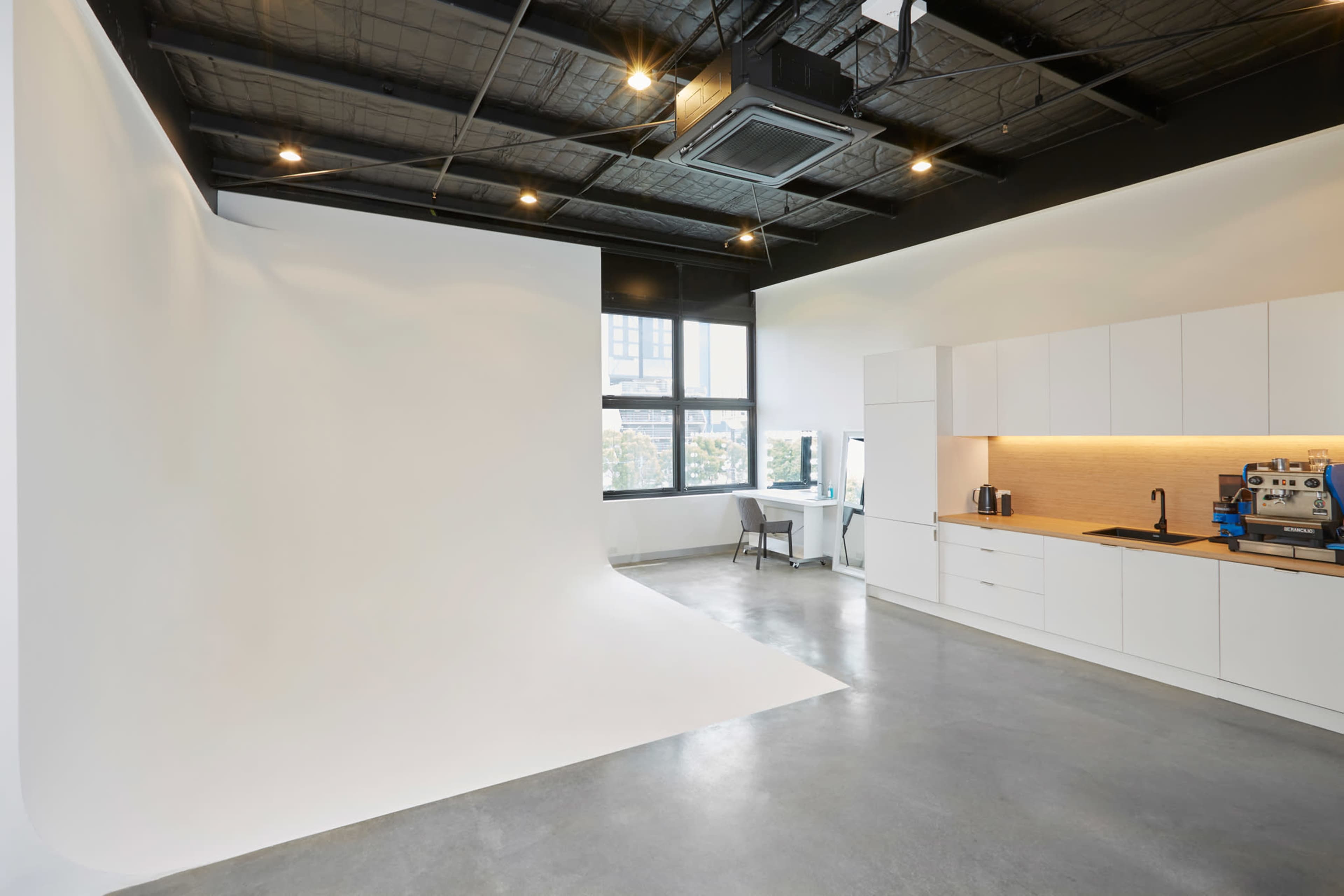 A bright studio space with a seamless white backdrop on one side and a modern kitchen area with cabinetry and appliances on the other.