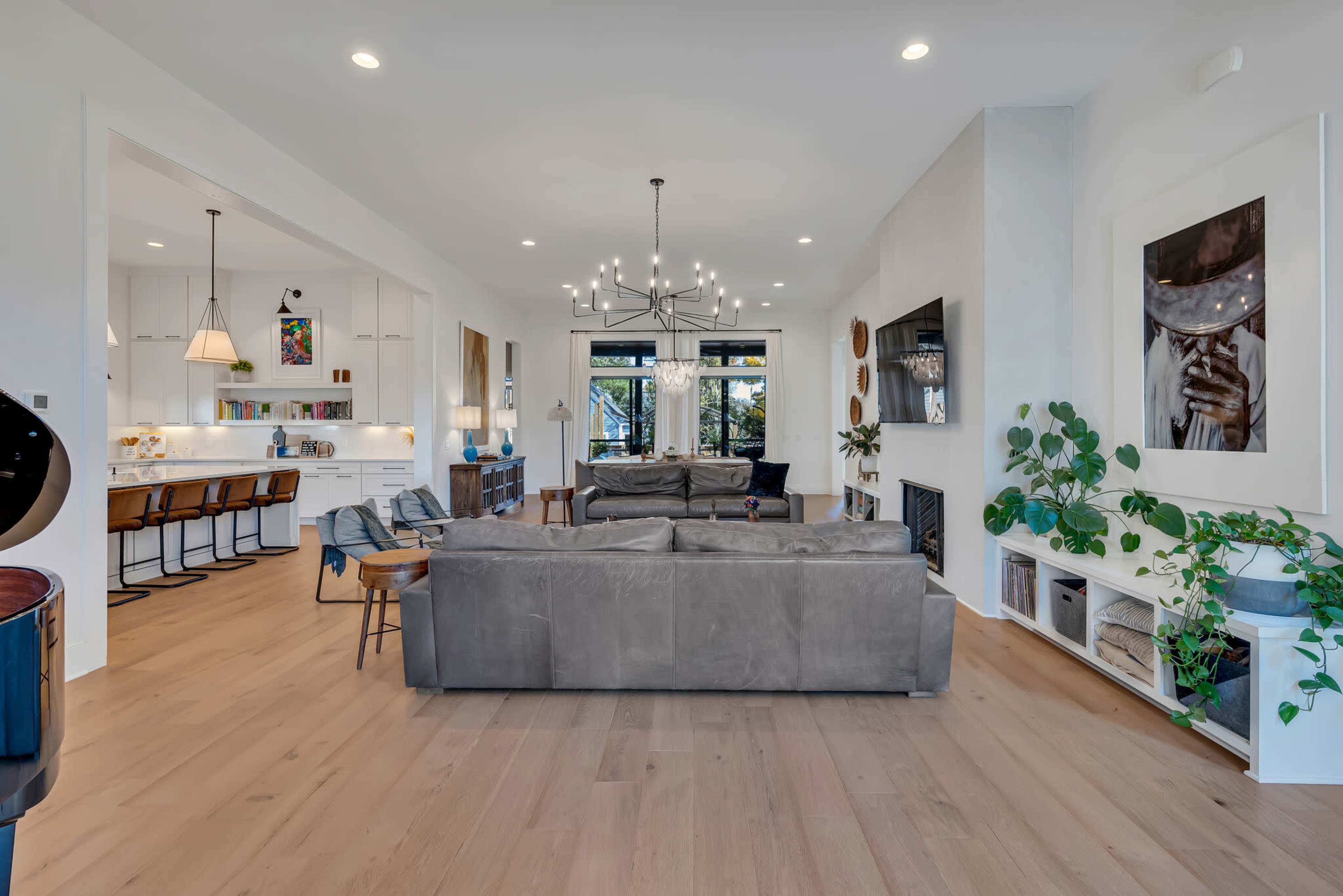 A modern living room with a large gray sectional sofa, a dining area in the background, and a bright, open layout featuring plants and contemporary decor.