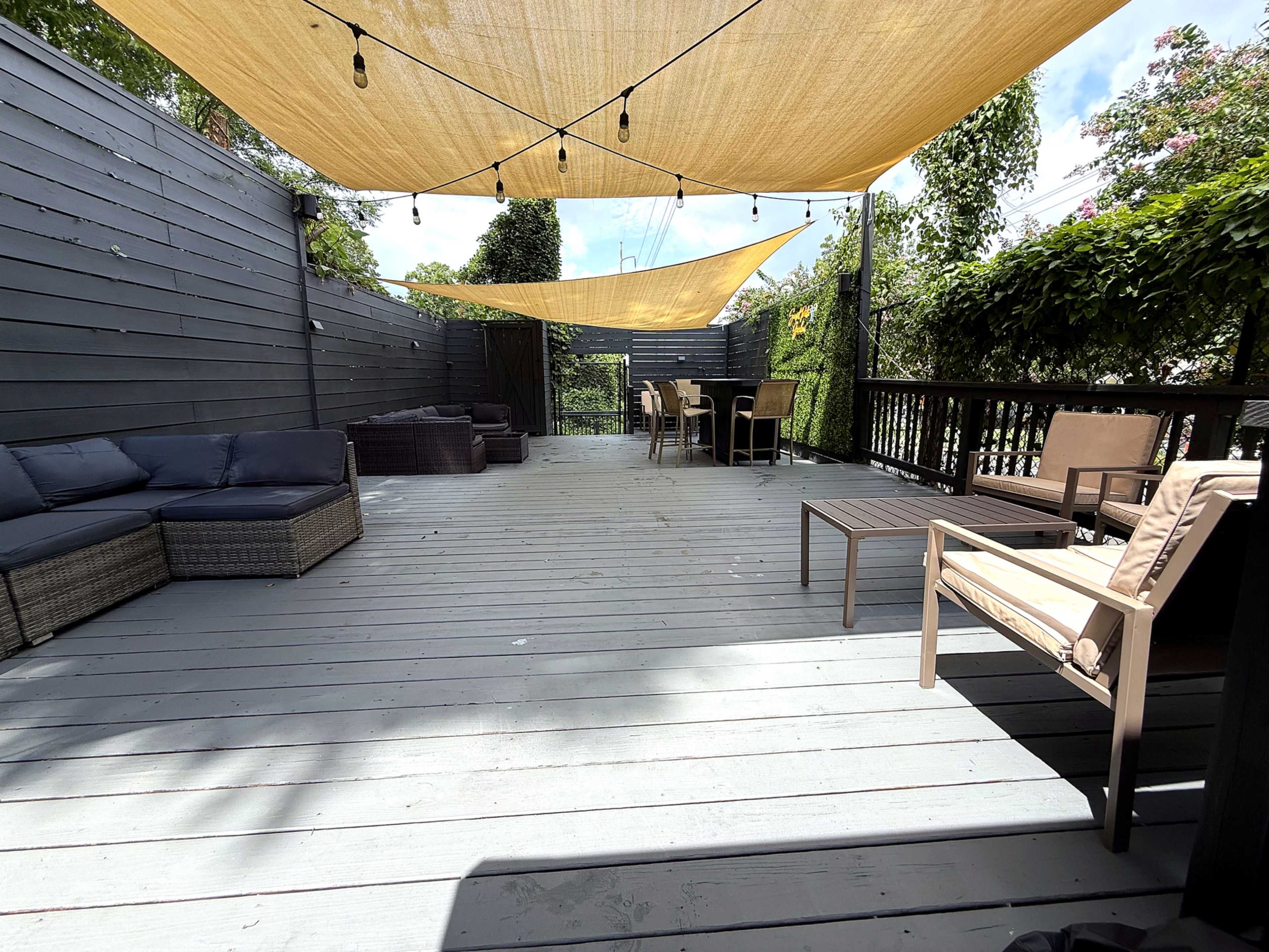 A spacious outdoor deck with shaded areas, featuring seating arrangements and a dining table surrounded by greenery.