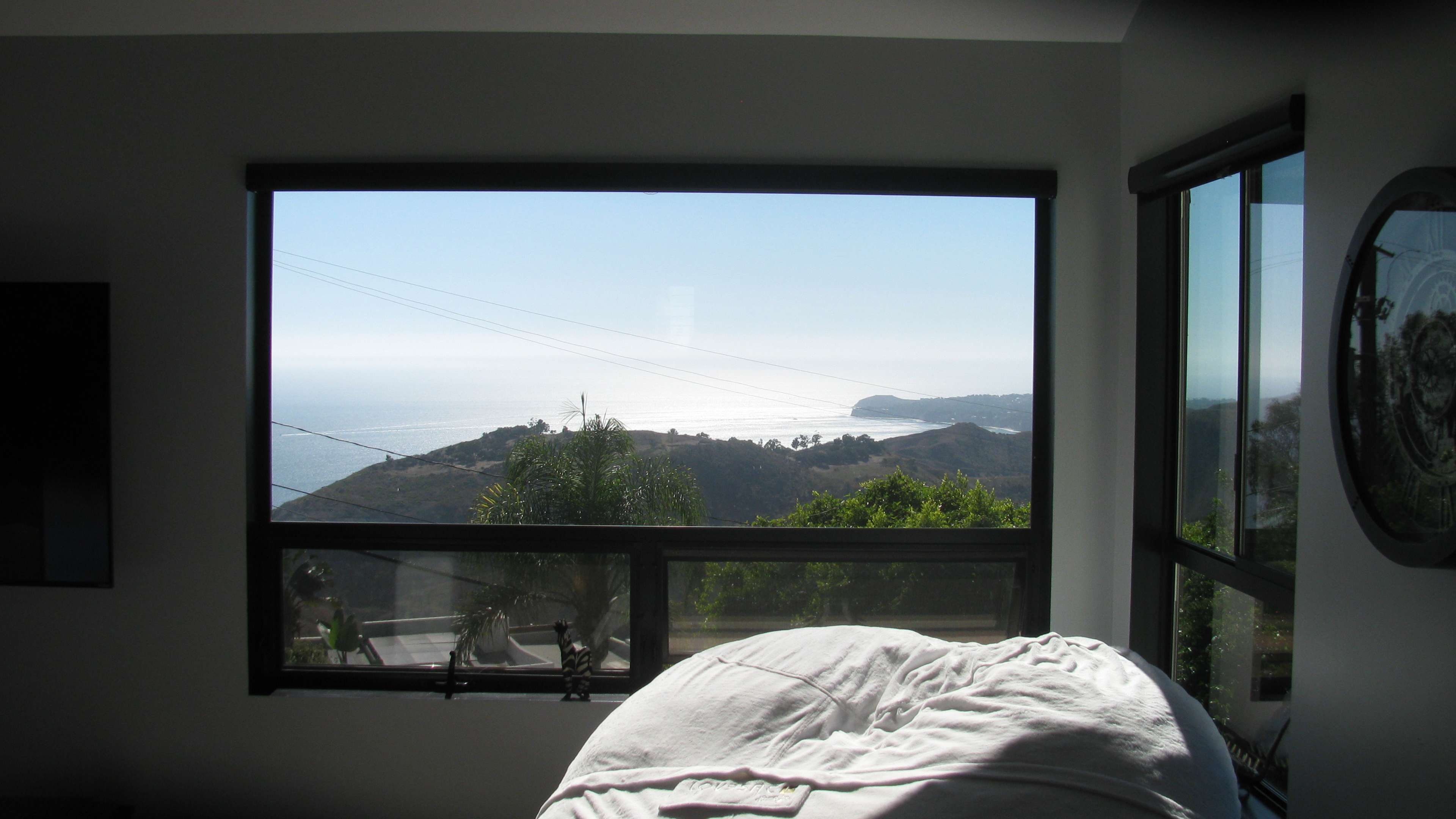A large window framing a view of the ocean and coastline, with a bed in the foreground.
