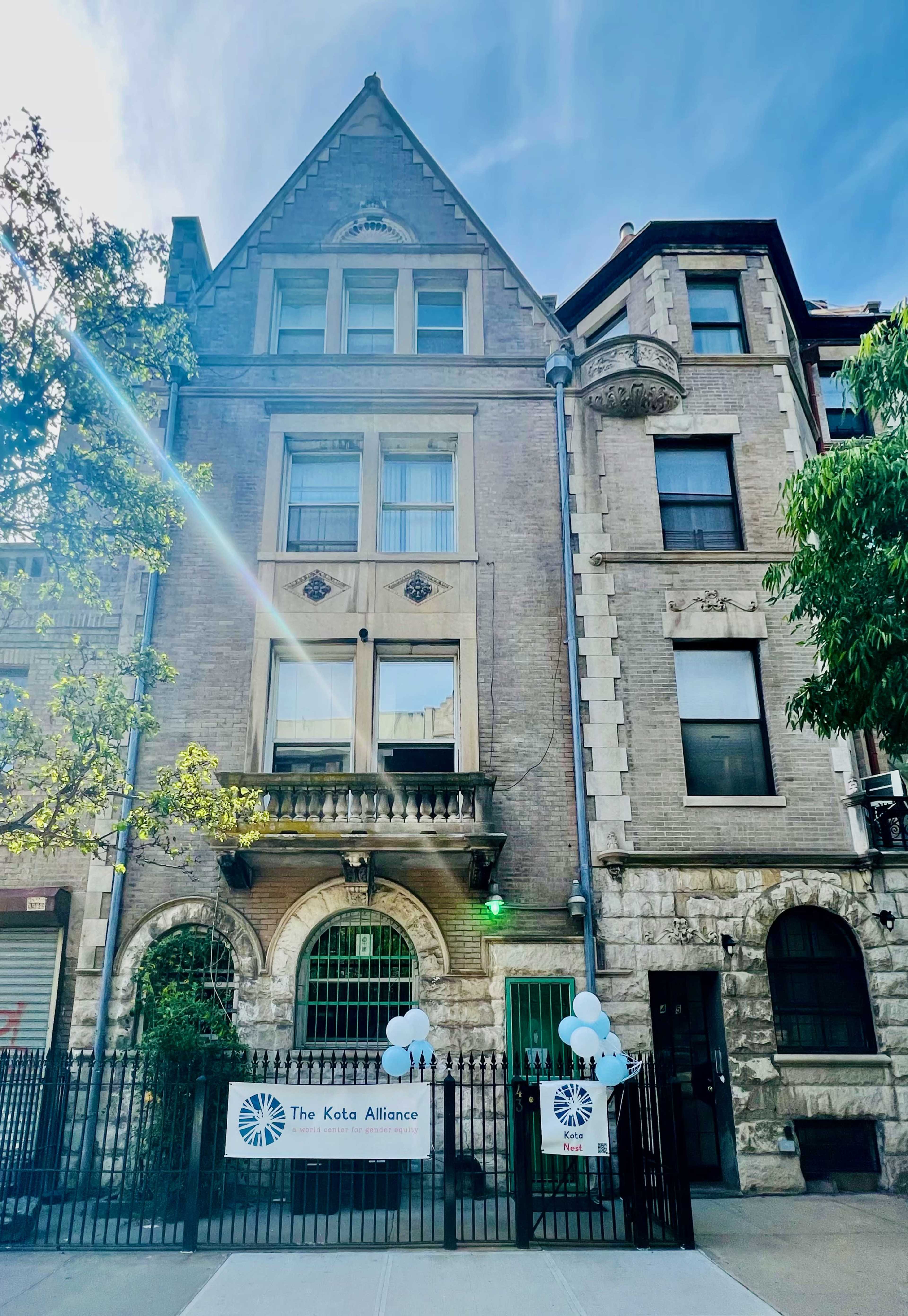 The image shows a multi-story brick building featuring architectural details like ornate windows and a balcony, with a banner for "The Keto Alliance" displayed outside along with blue balloons.