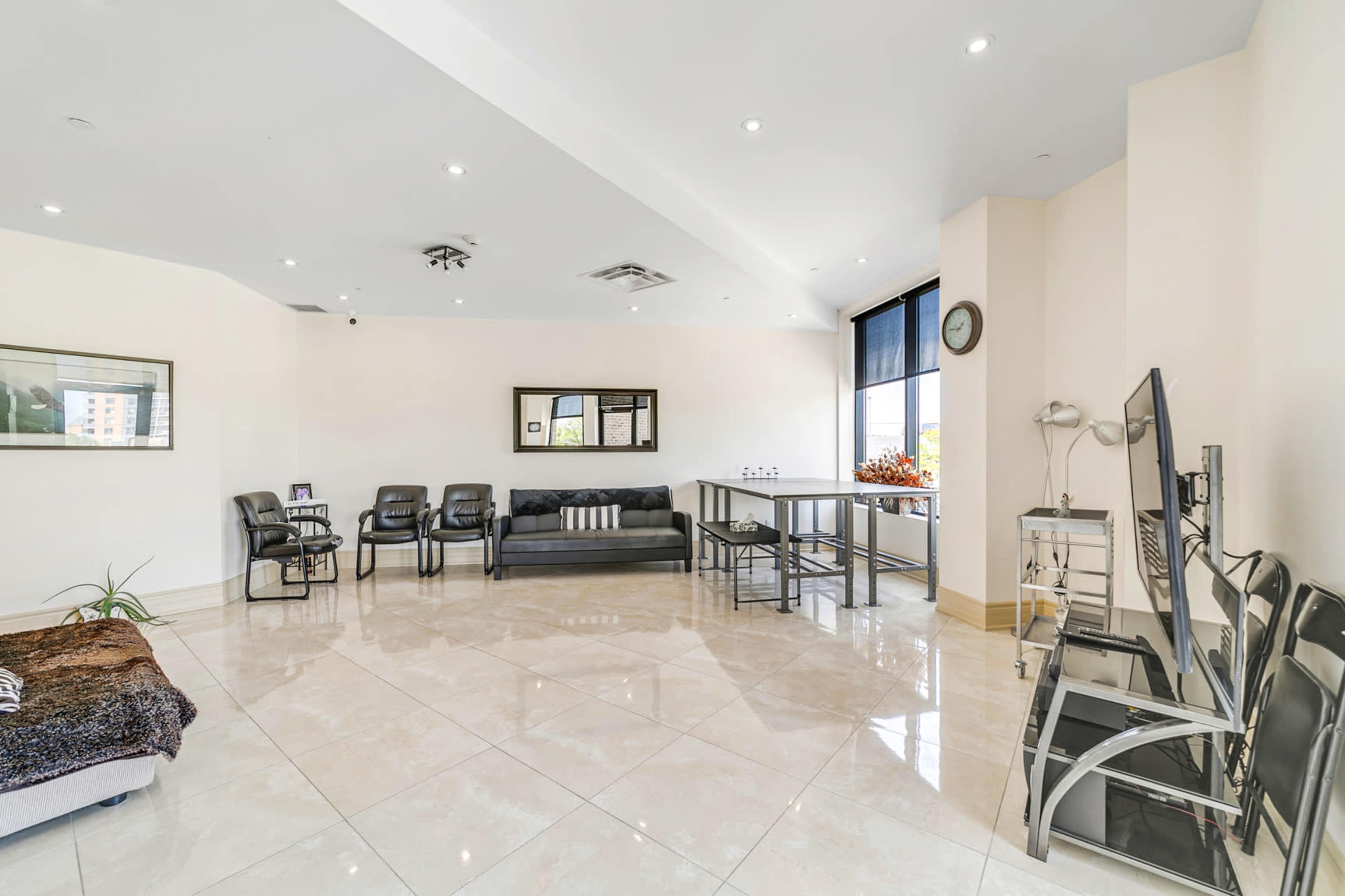 The image shows a spacious, well-lit waiting area furnished with chairs, a sofa, and a small kitchenette along one wall.