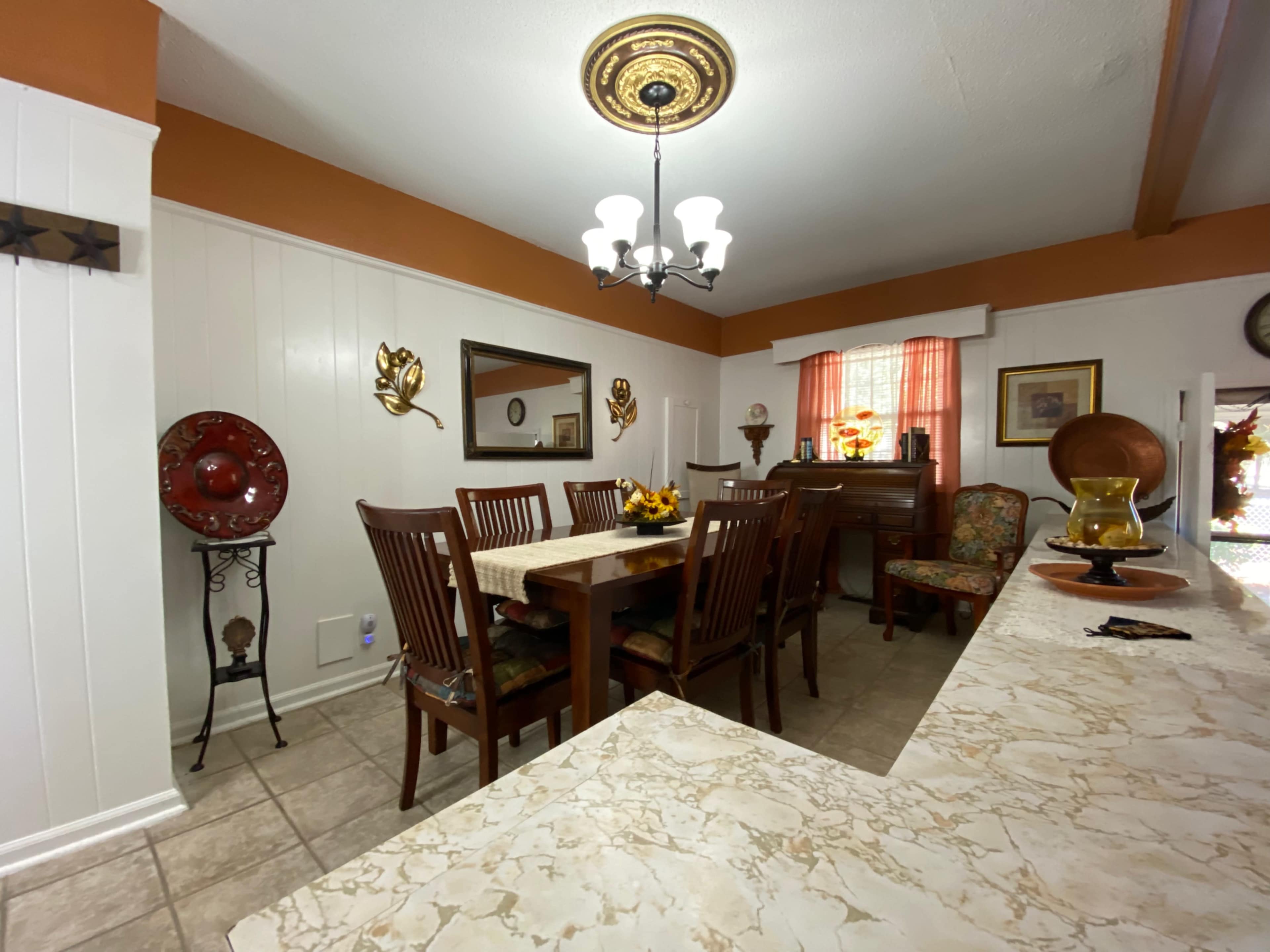 A dining area with a wooden table surrounded by chairs, a piano in the background, and decorative items on the walls.