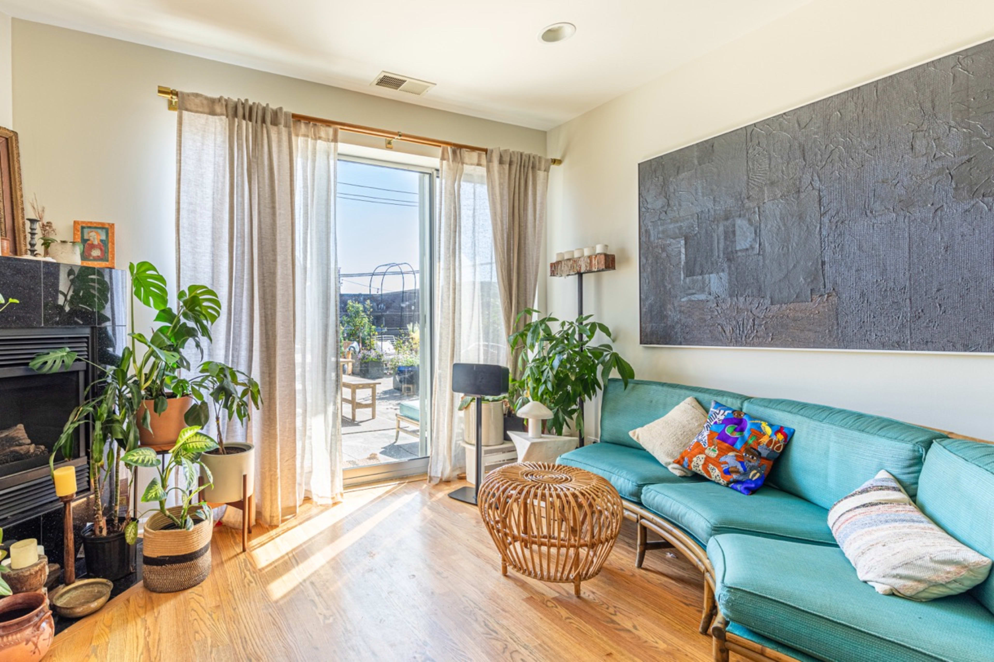 A bright living room features a teal sofa, potted plants, a round coffee table, and a glass door leading to an outdoor area.