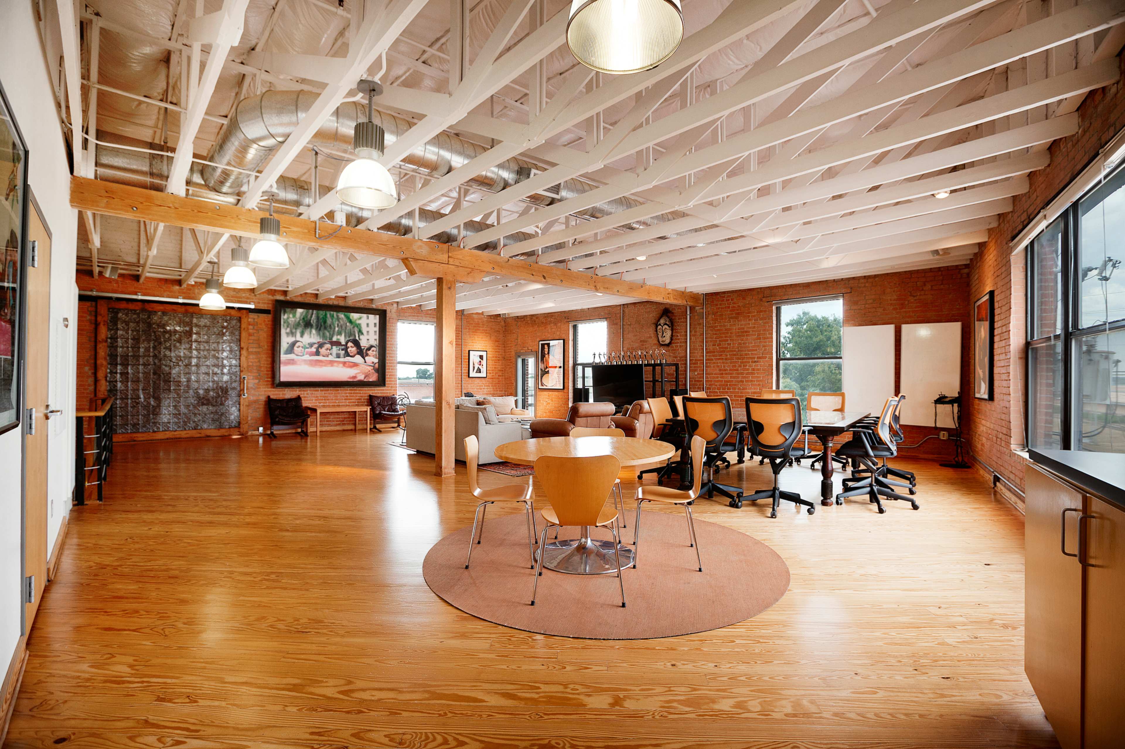 A spacious, modern office interior with wooden floors, exposed beams, and large windows.