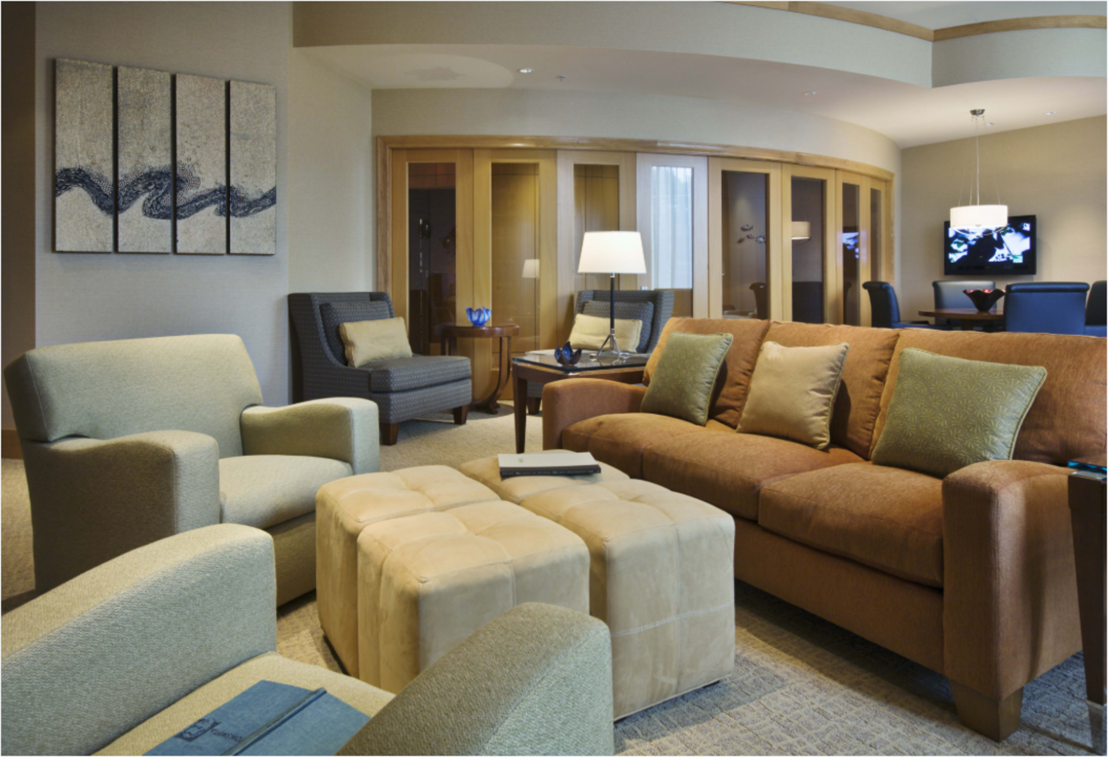 The image shows a modern living area with two armchairs, a brown sofa, a coffee table, and a lamp, set in a well-lit room featuring a television in the background.