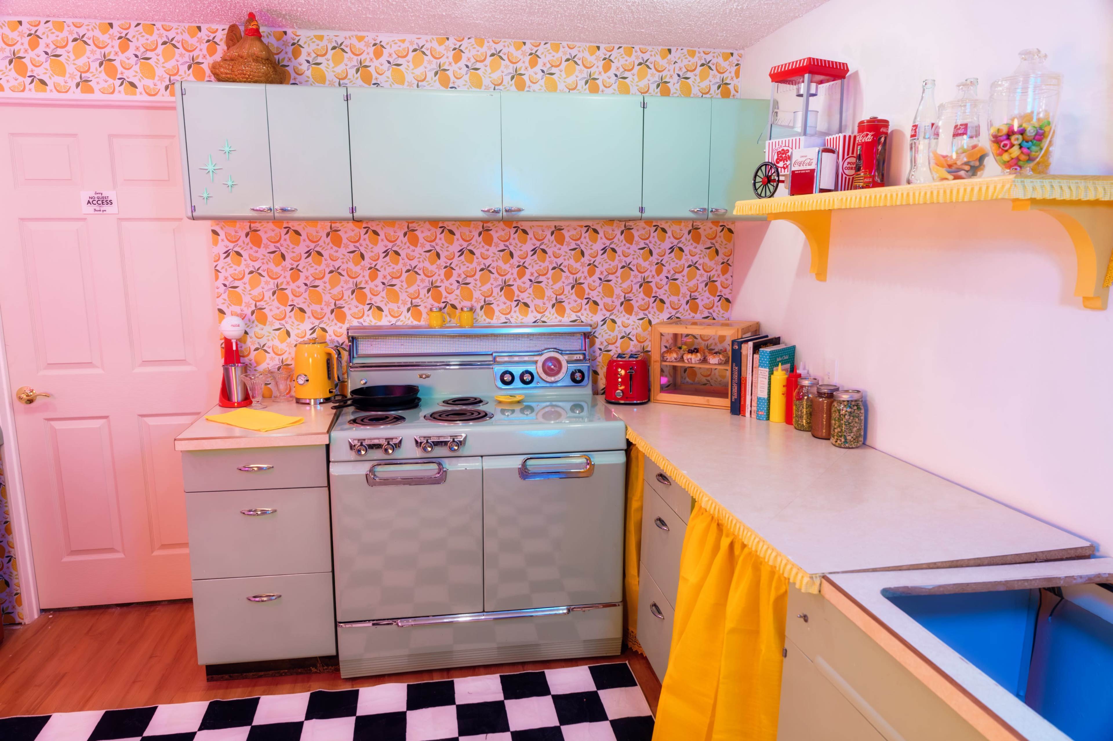 The image shows a vintage-style kitchen with mint green cabinets, a checkered floor, and lemon-themed wallpaper.