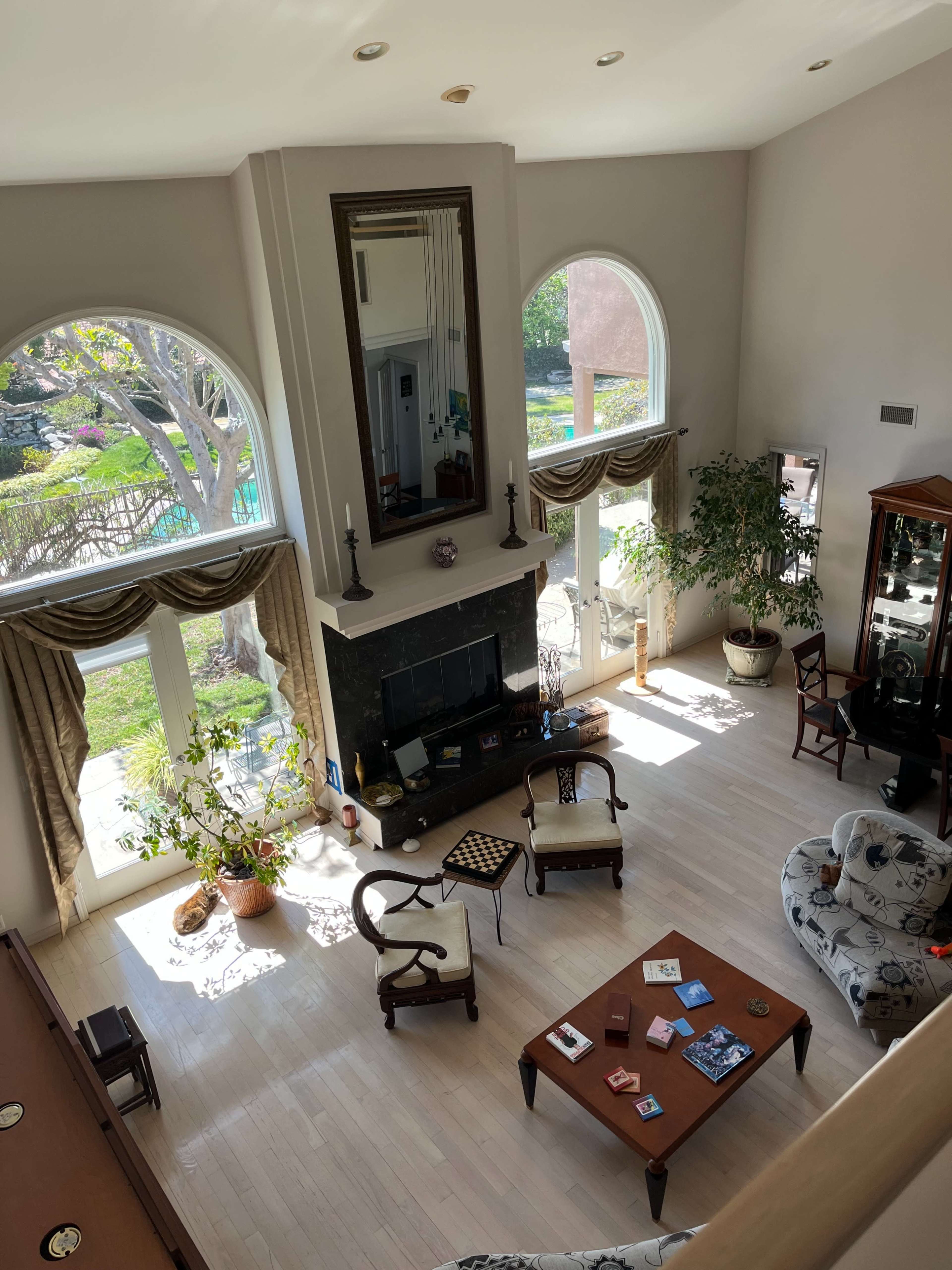 The image shows a spacious living room with large windows, a fireplace, and various pieces of furniture including chairs and a coffee table.