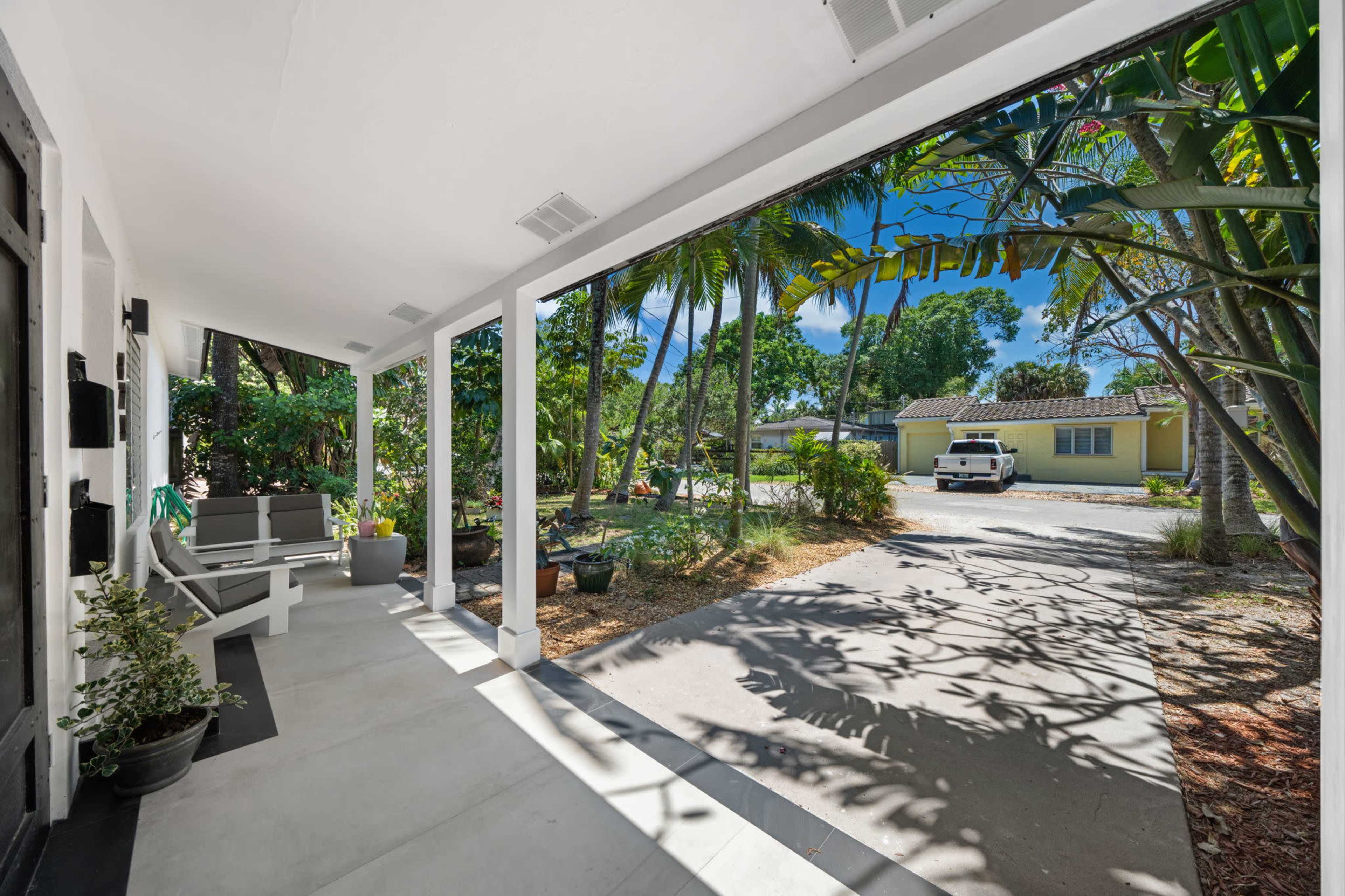 A covered porch with a view of a driveway and several trees in a residential area.