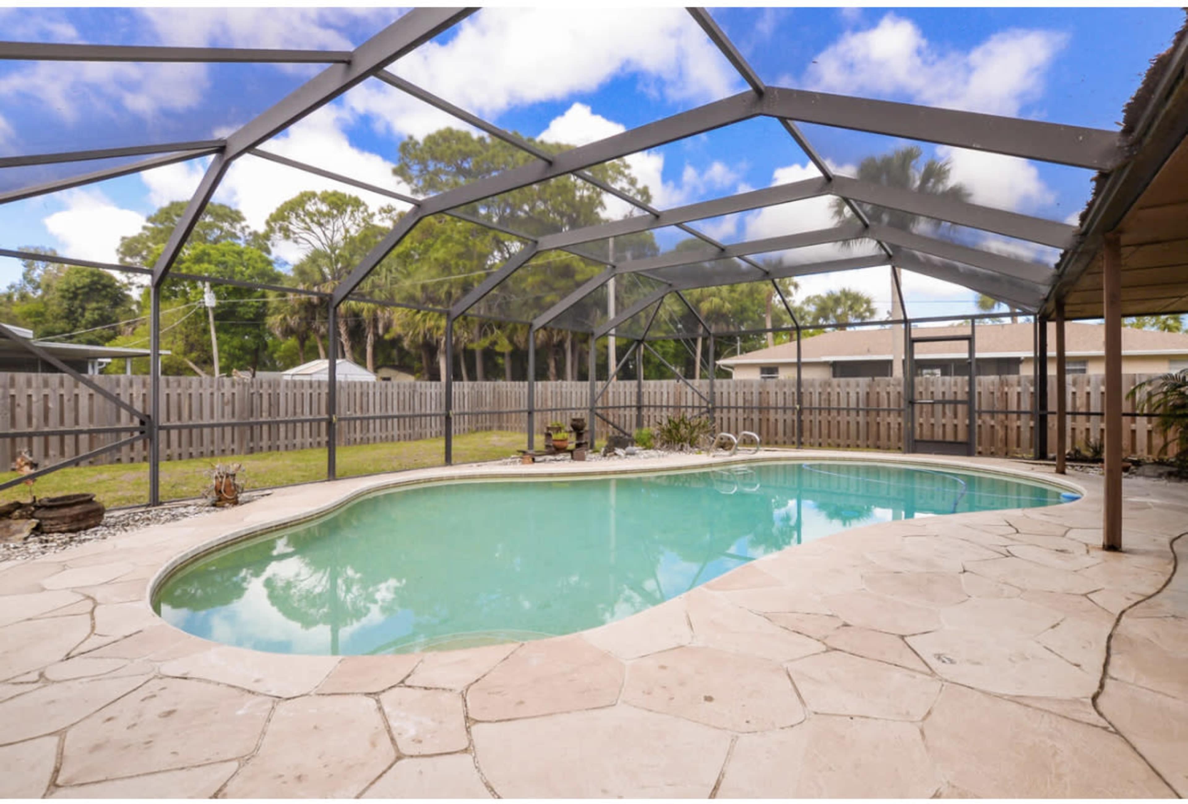 A backyard swimming pool enclosed by a screen enclosure, surrounded by a stone deck and landscaped yard.