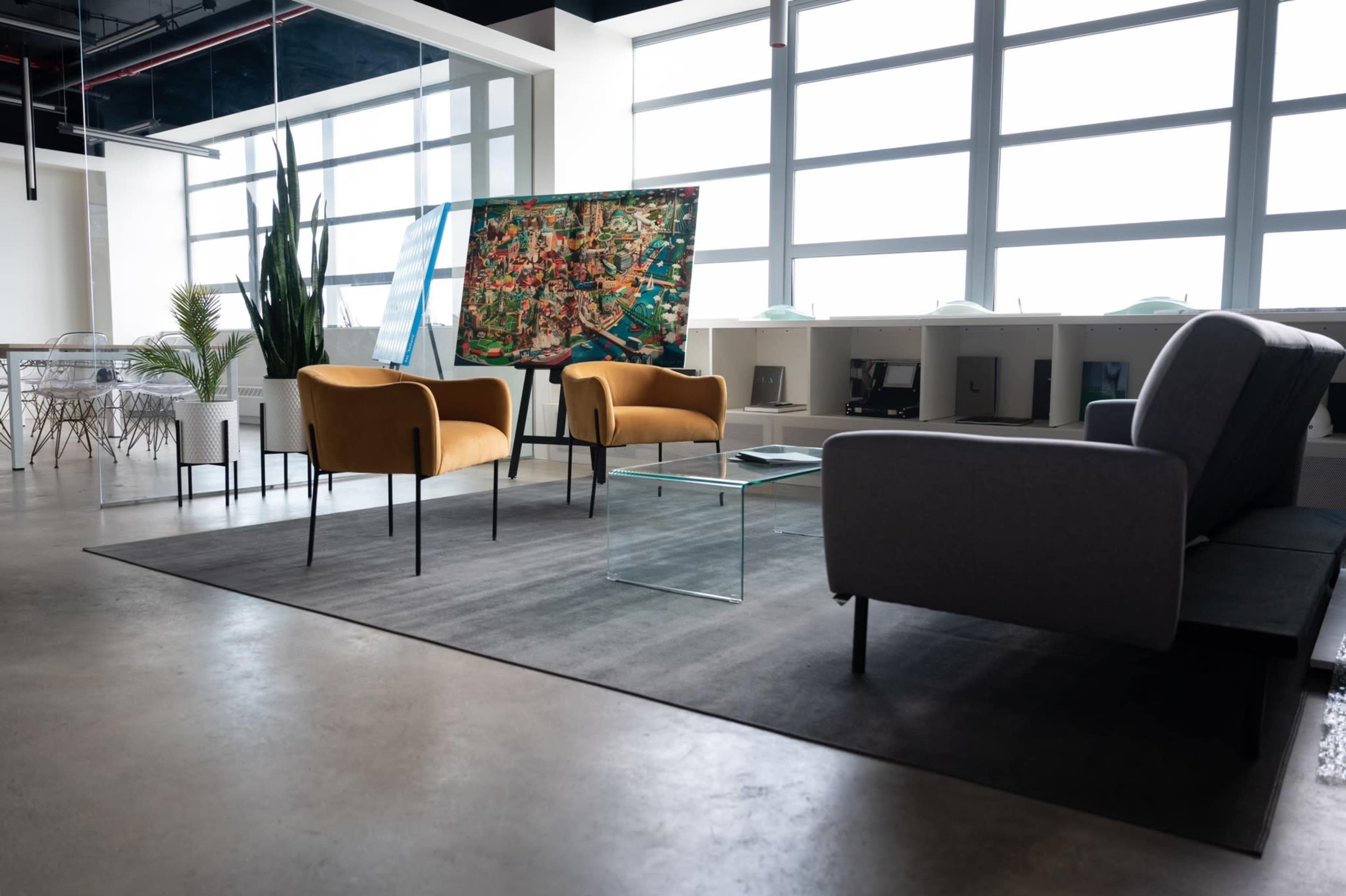 A modern office space with two mustard-colored chairs, a glass coffee table, a gray sofa, and a large map displayed on an easel.
