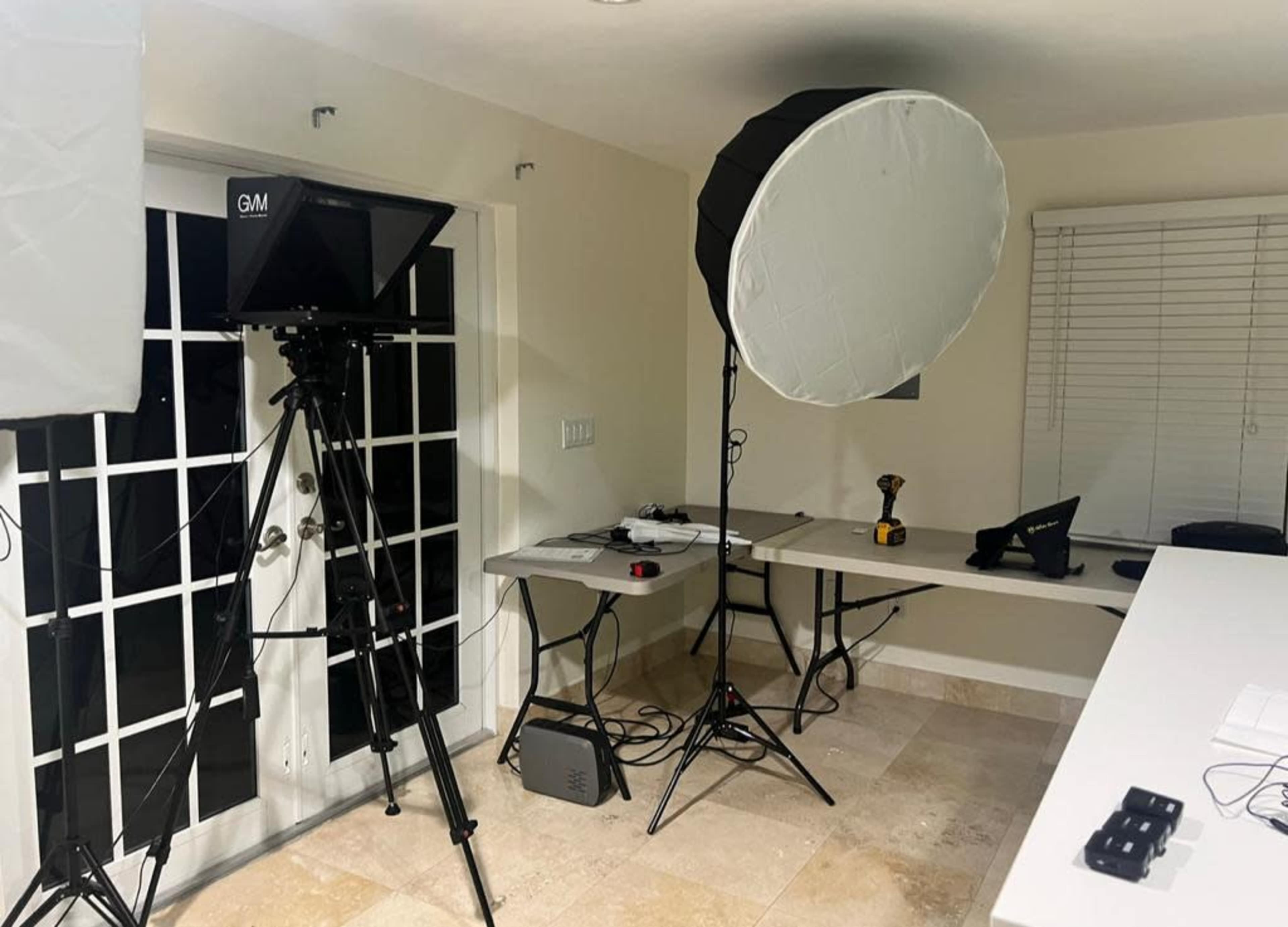 A well-lit indoor studio setup with a camera on a tripod, a large softbox light, and several tables with equipment.