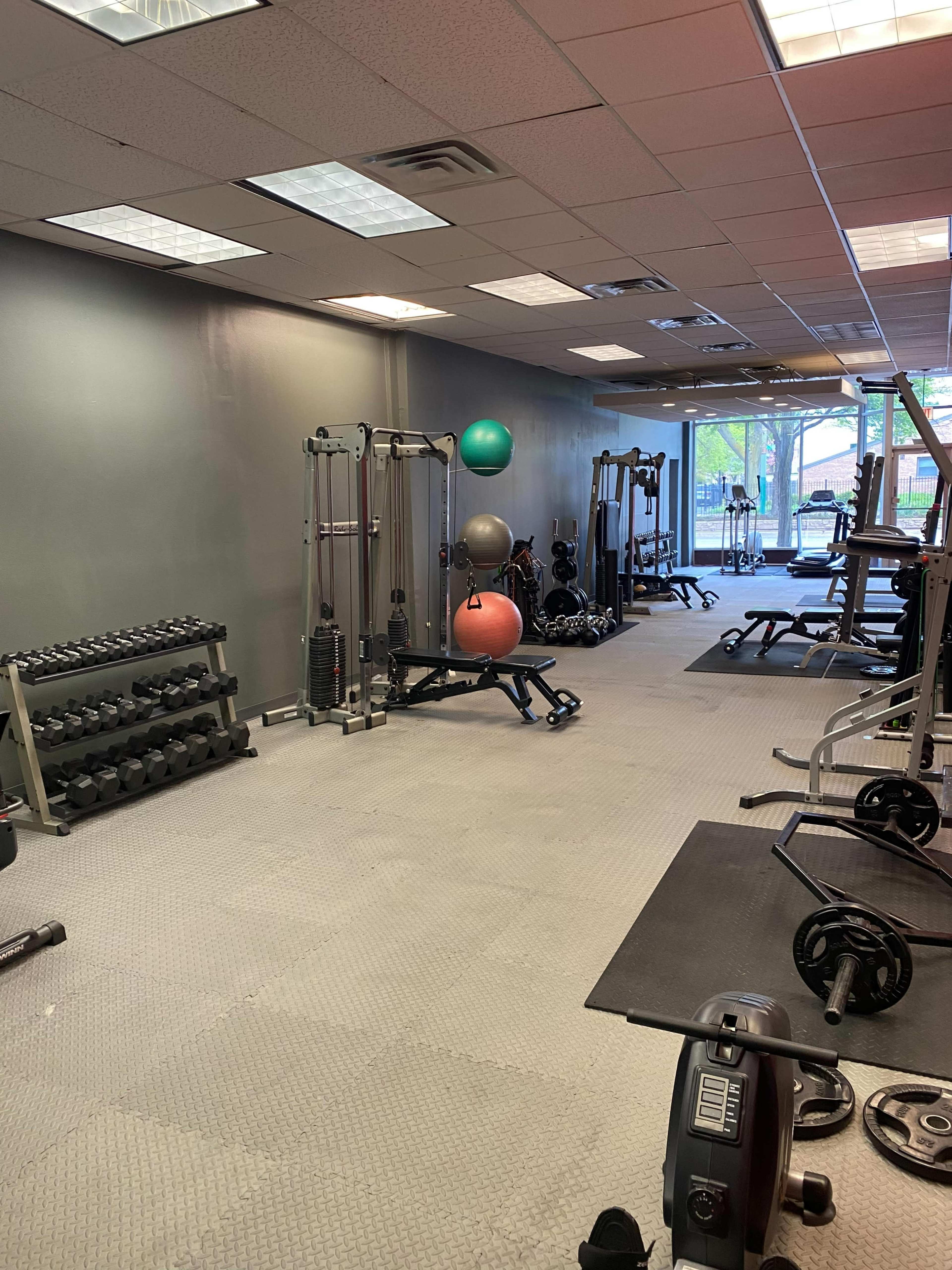 The image shows a gym interior with various fitness equipment, including weights, exercise balls, and machines.