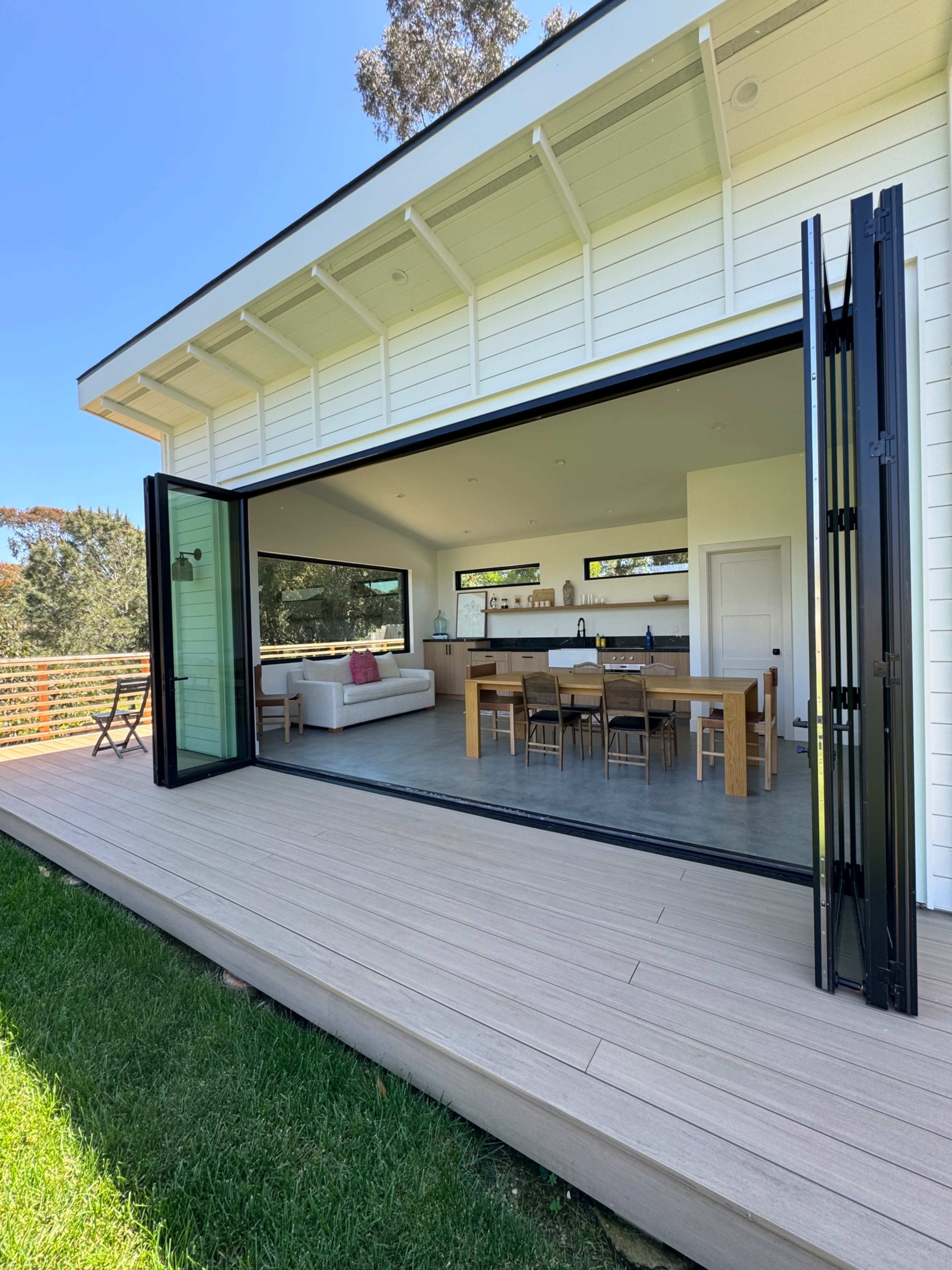 A modern house features large open doors leading to a spacious indoor dining area with a view of the outdoor decking.