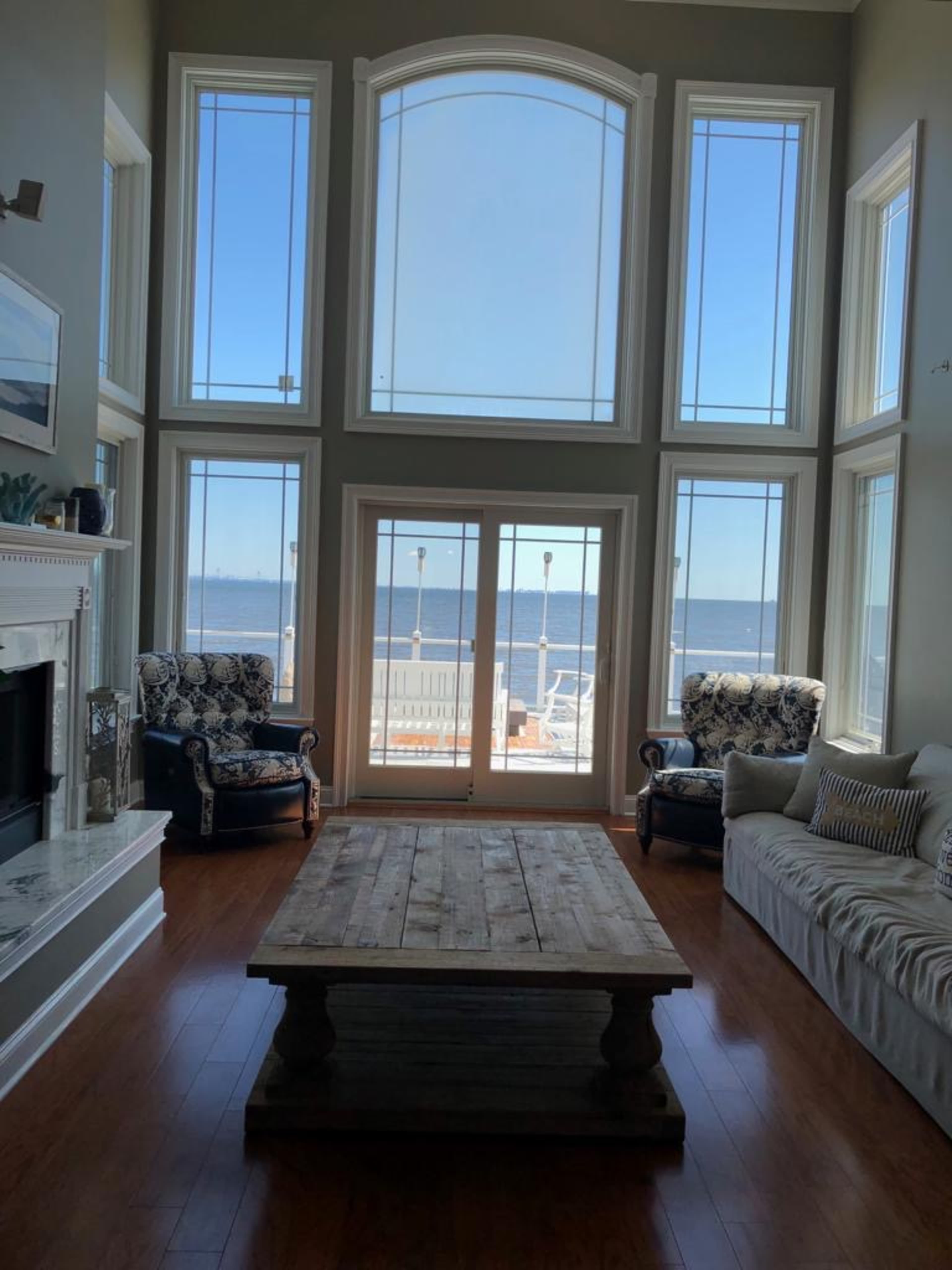 A living room with large windows overlooking a body of water, featuring two armchairs and a wooden coffee table.