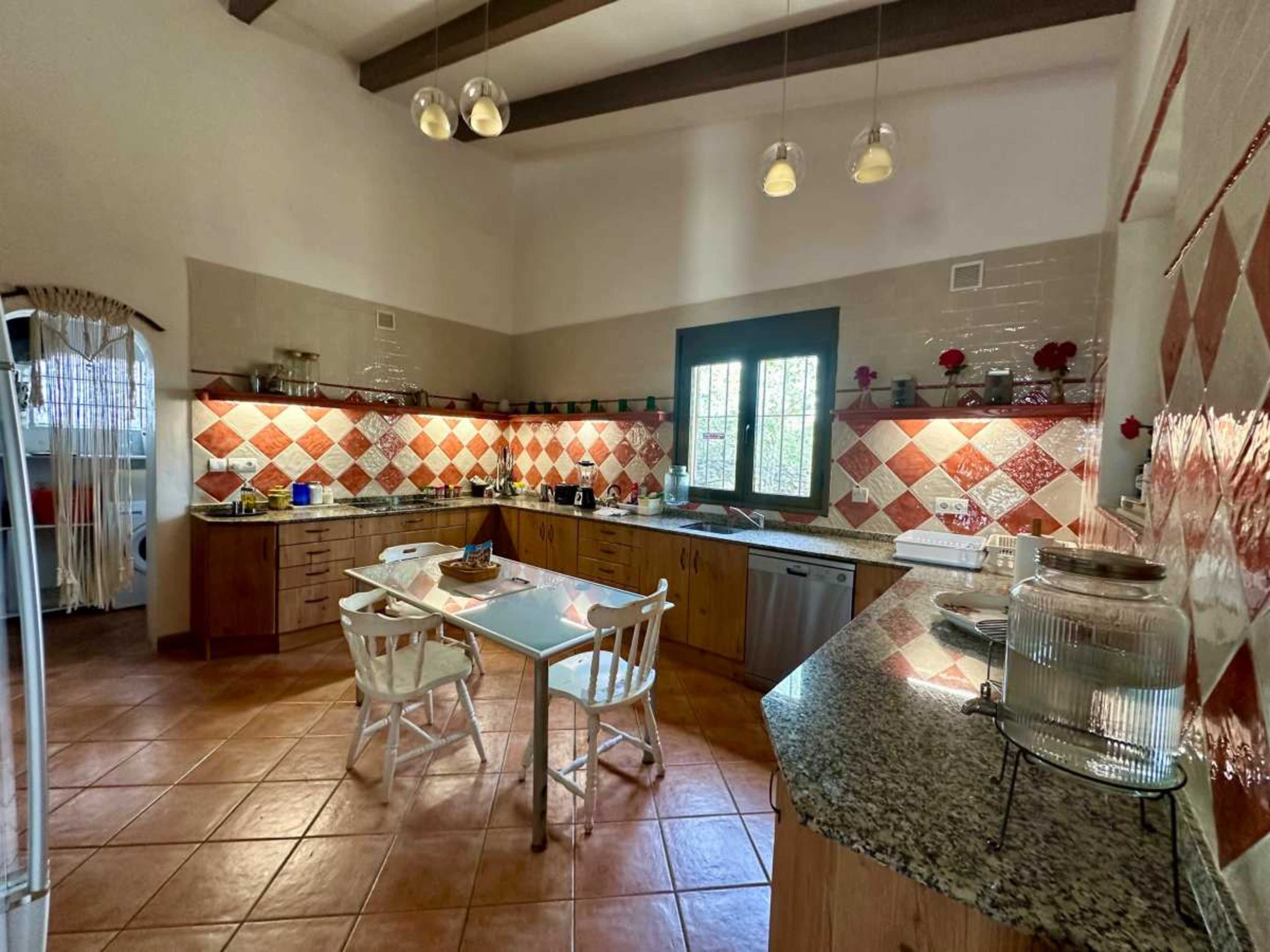 The kitchen features wooden cabinets, a tiled backsplash with a diamond pattern, and a dining table surrounded by white chairs.