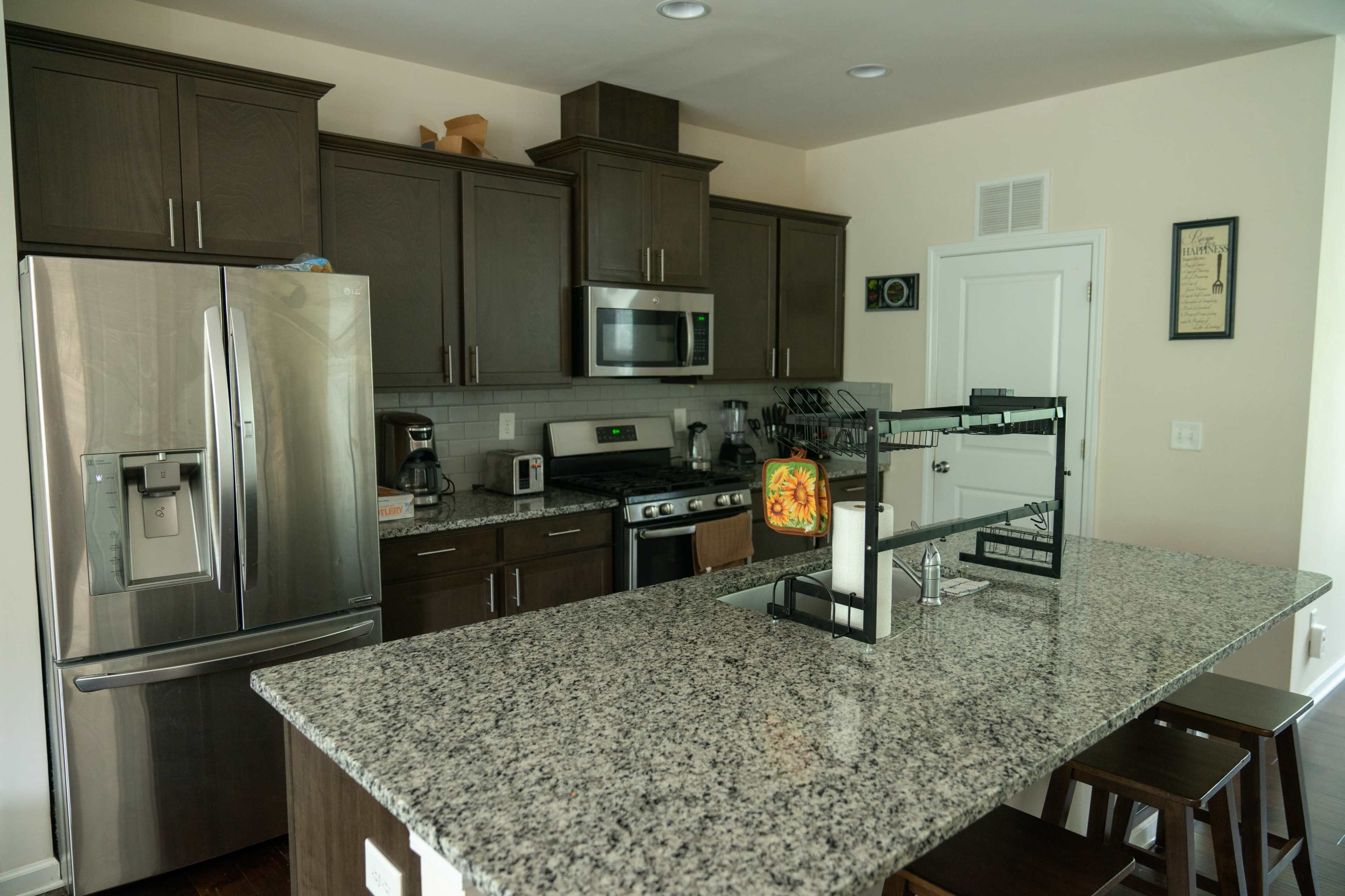 The kitchen features dark wood cabinets, stainless steel appliances, and a large granite island with seating.
