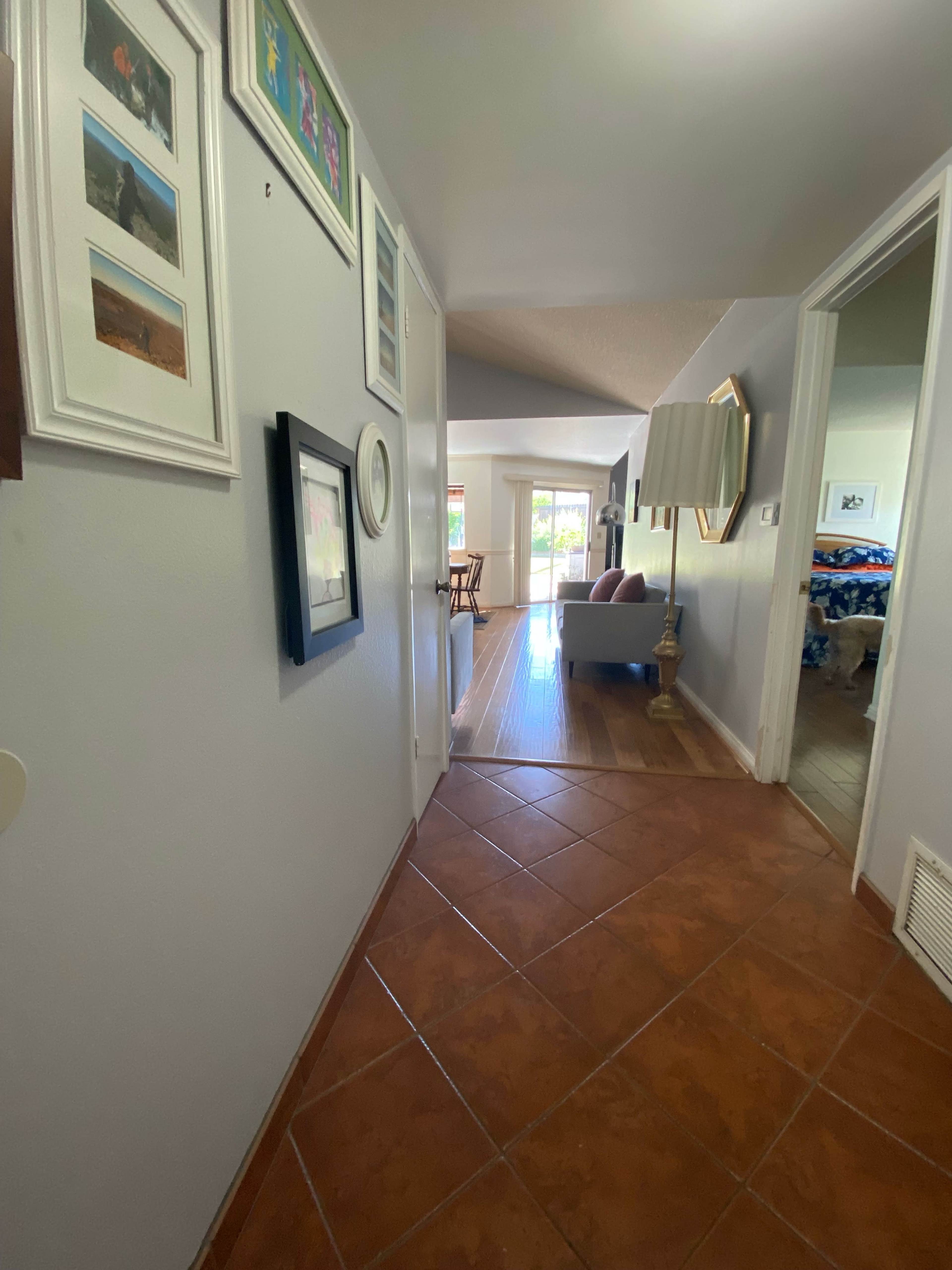 A hallway with framed photographs on the walls, leading to a living area and an open door at the end.