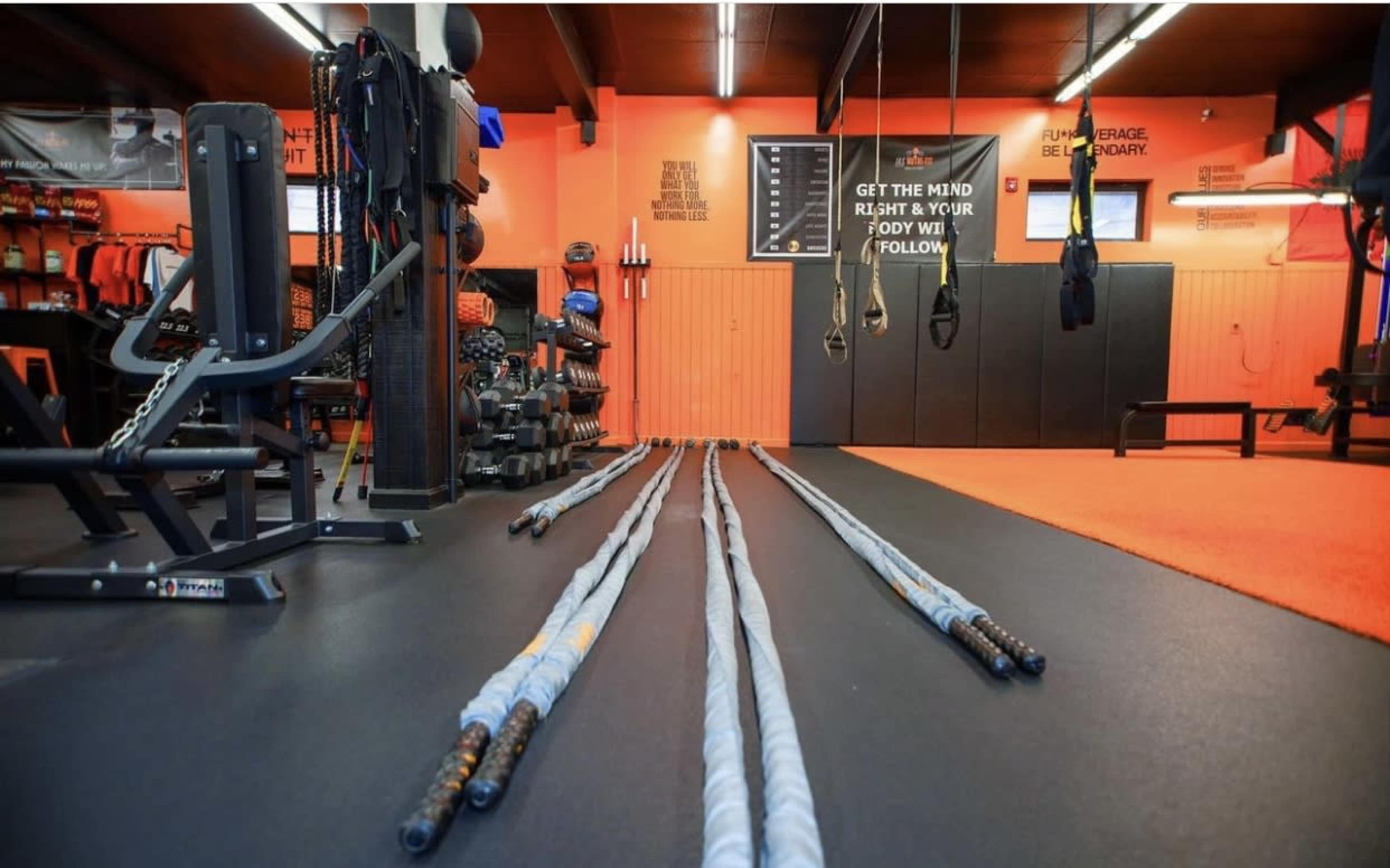 A well-equipped gym interior with various workout equipment and battle ropes laid out on the floor.