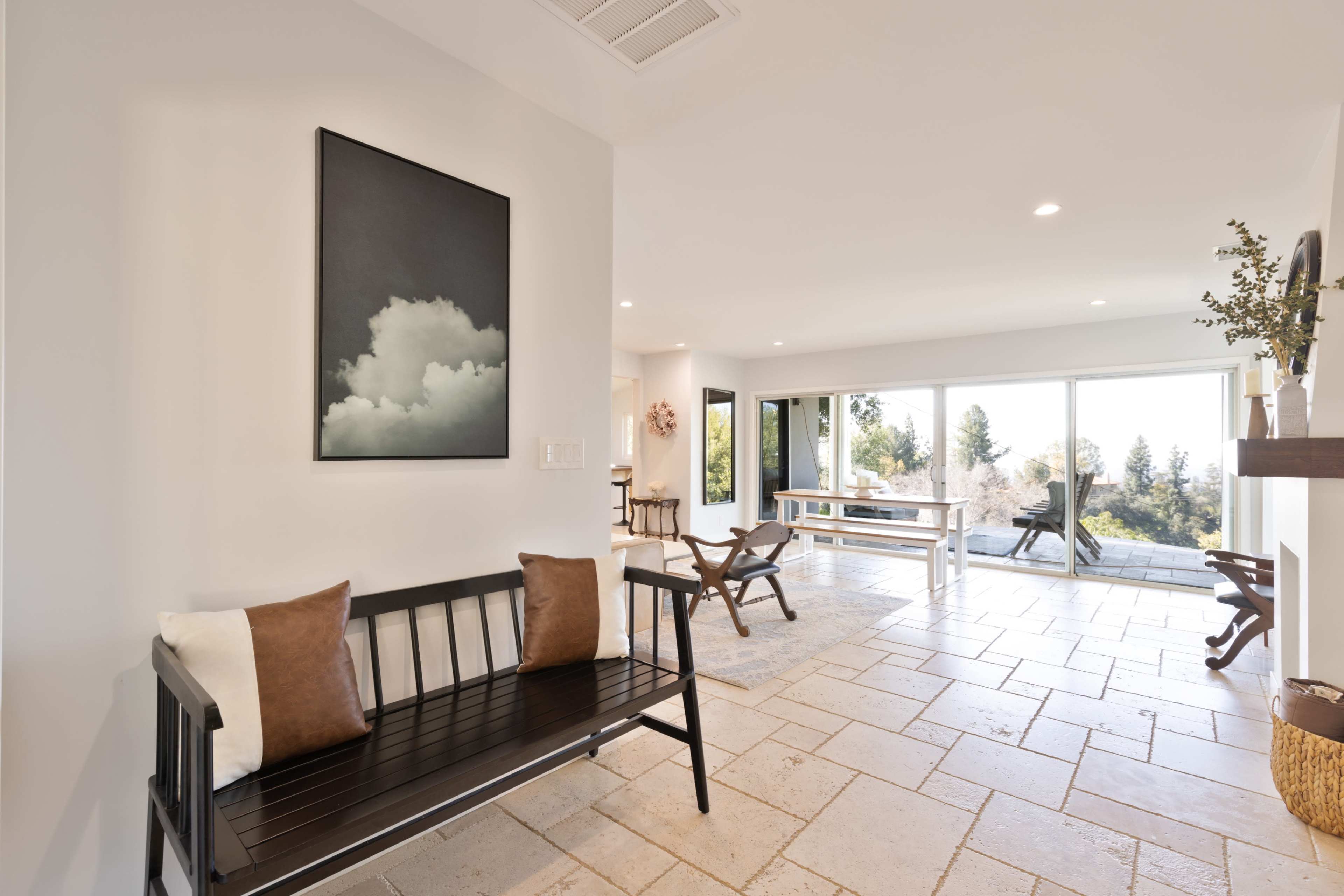 A modern interior features a black bench with pillows, a table, and large windows overlooking a natural landscape.