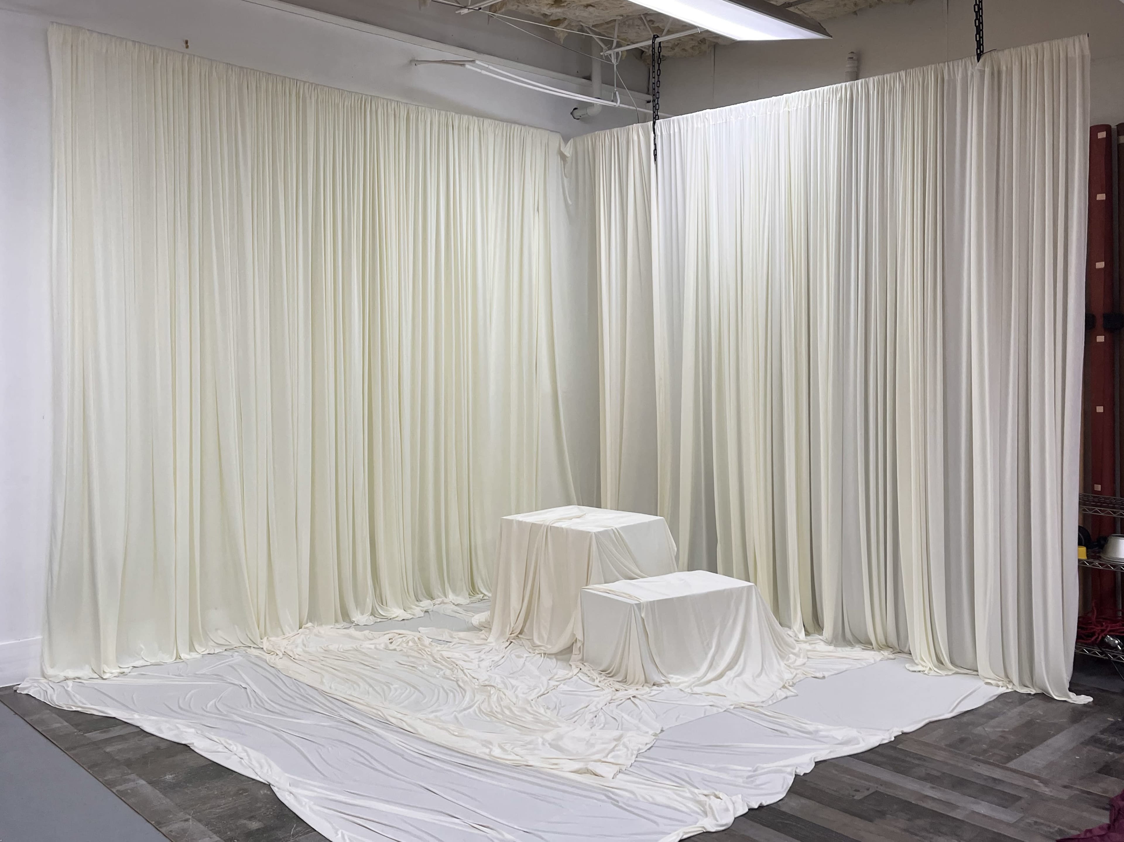 The image shows a studio space with white fabric draped along the walls and two white pedestals placed on a fabric-covered floor.