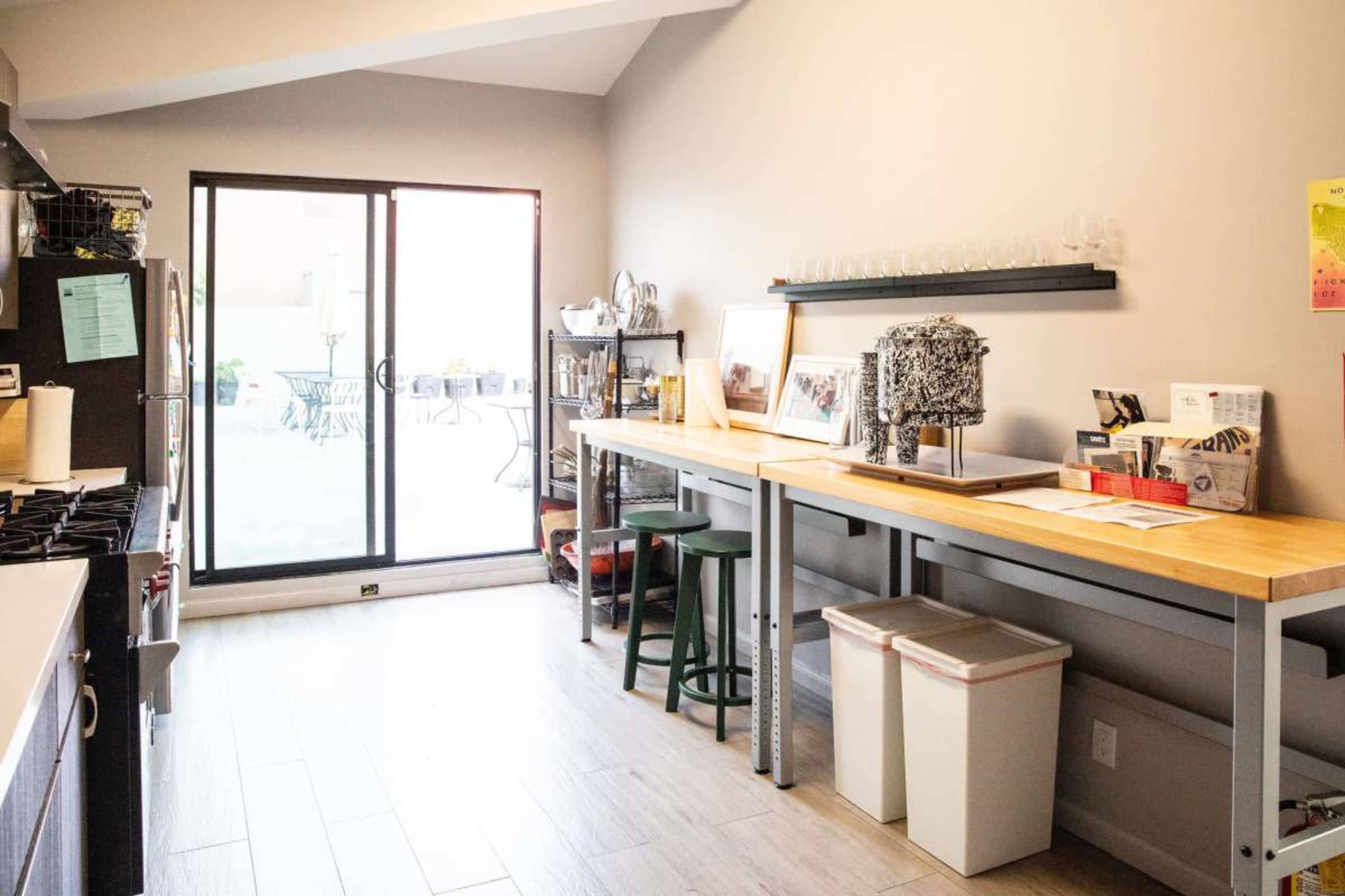A modern kitchen features a long wooden counter, a large window with sliding glass doors, and a view of an outdoor patio with seating.