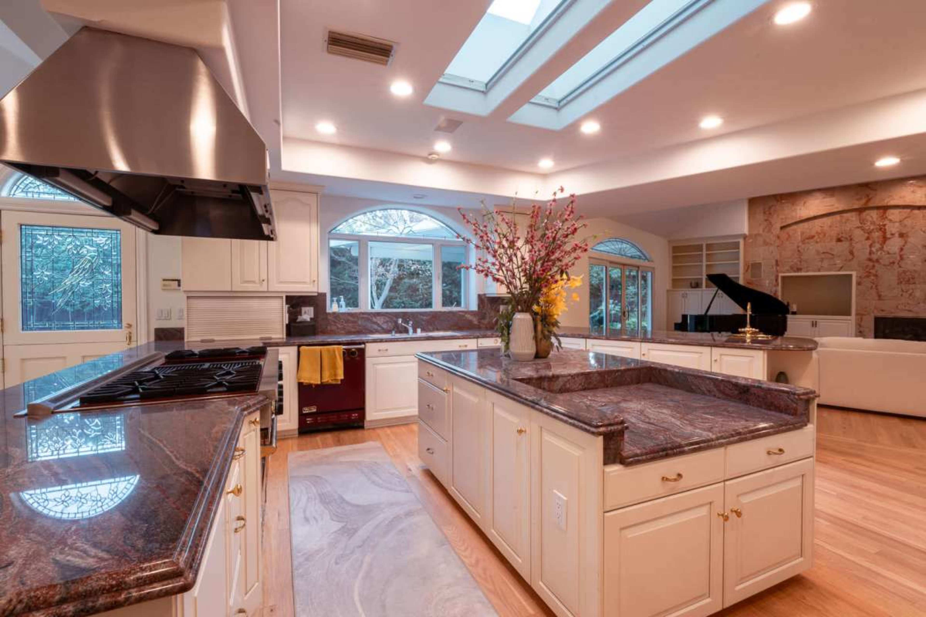 The kitchen features a large central island with a granite countertop, stainless steel appliances, and skylights that provide natural light.