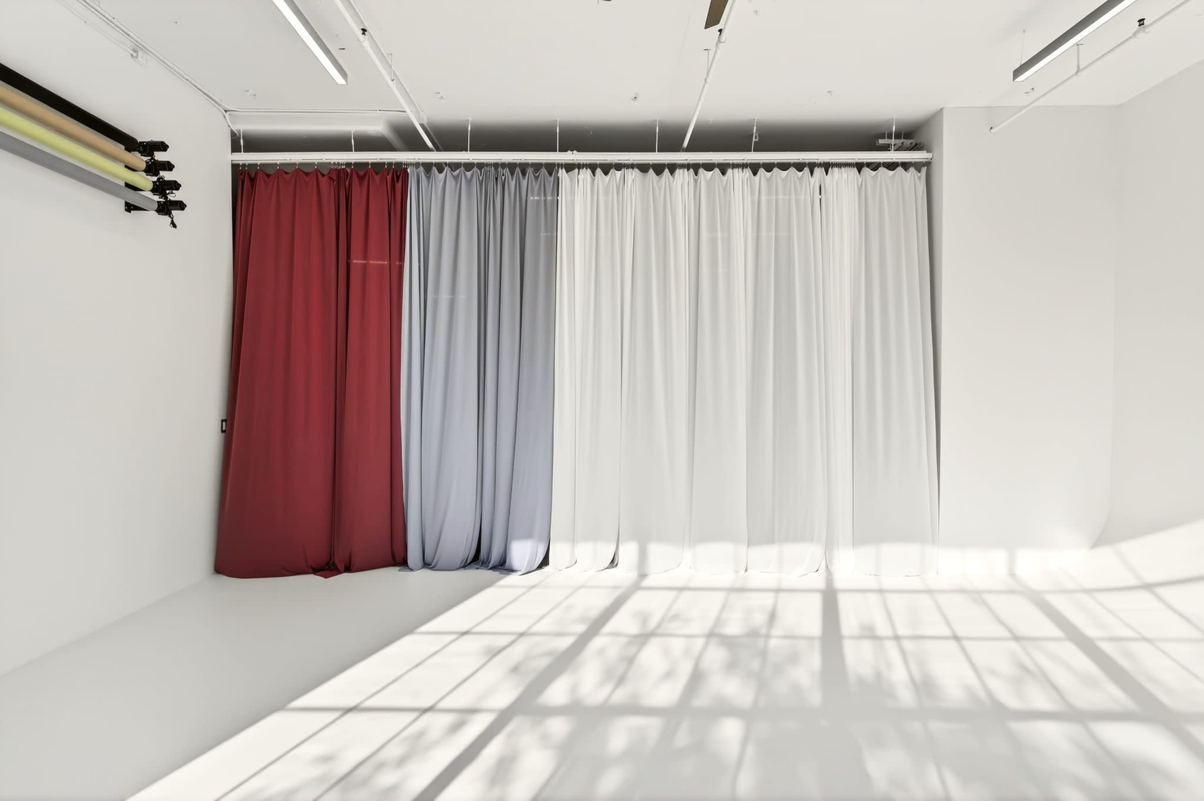 The image shows a studio space with three sections of curtains in red, gray, and white draped across a wall, casting shadows on a light-colored floor.