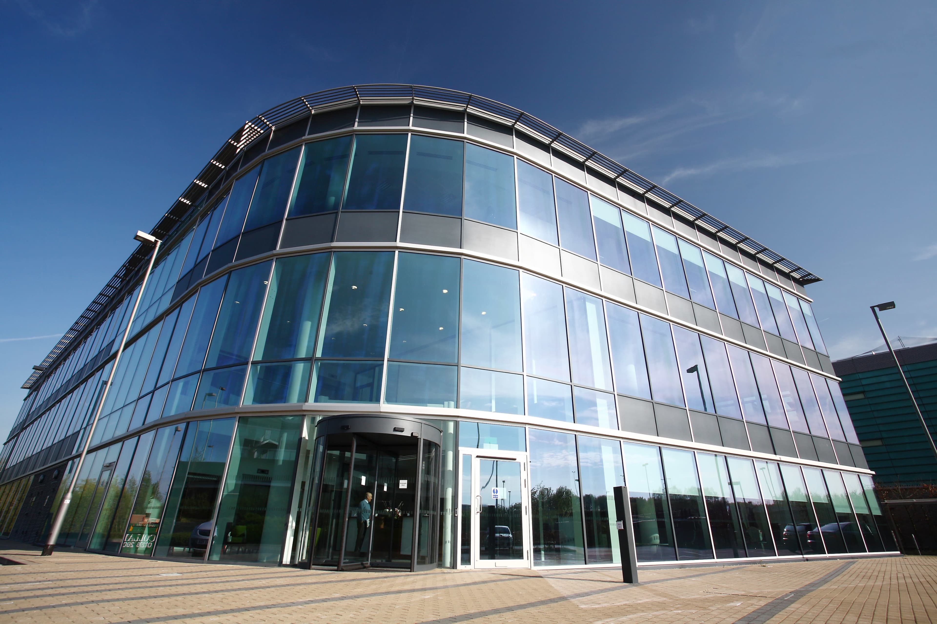 A modern glass building with a curved facade and a main entrance featuring revolving doors.