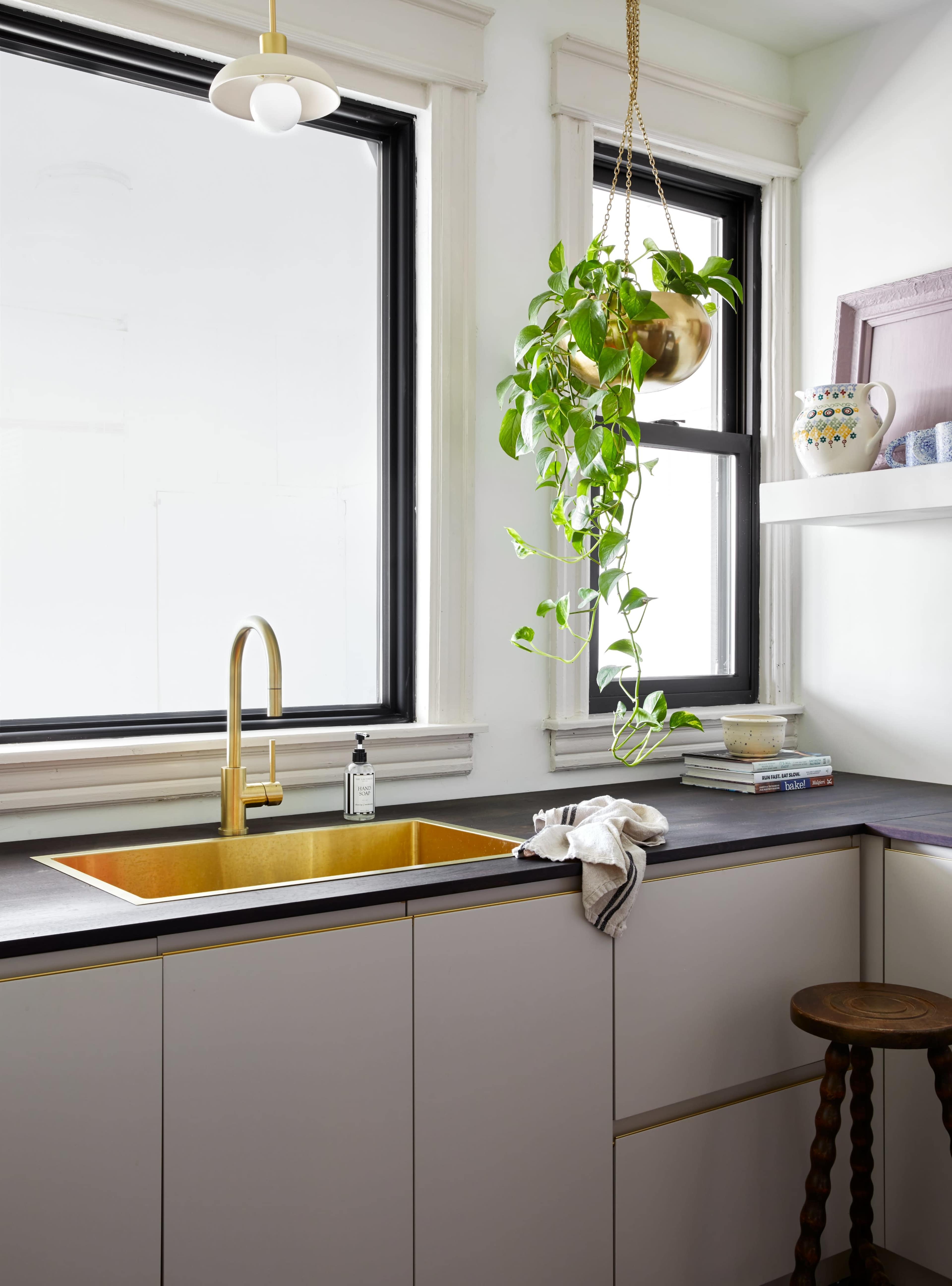 A modern kitchen features a gold sink, a hanging plant, and a window with natural light.